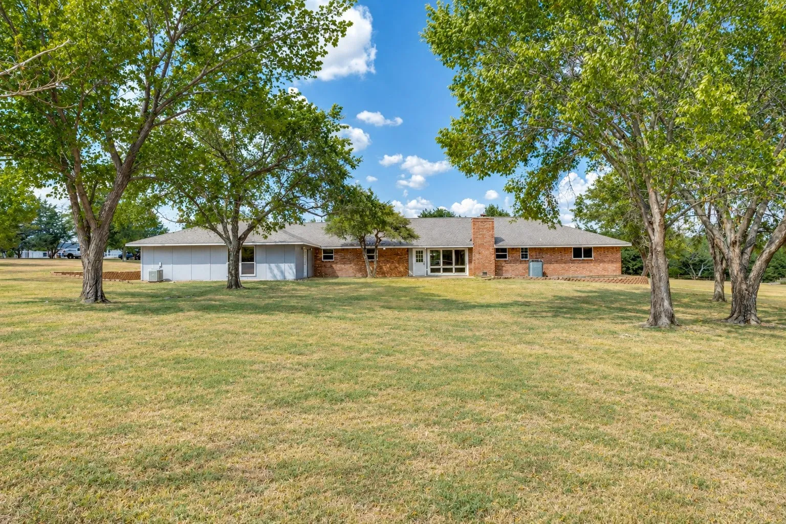 Expansive green space featuring mature trees and a brick and siding exterior
