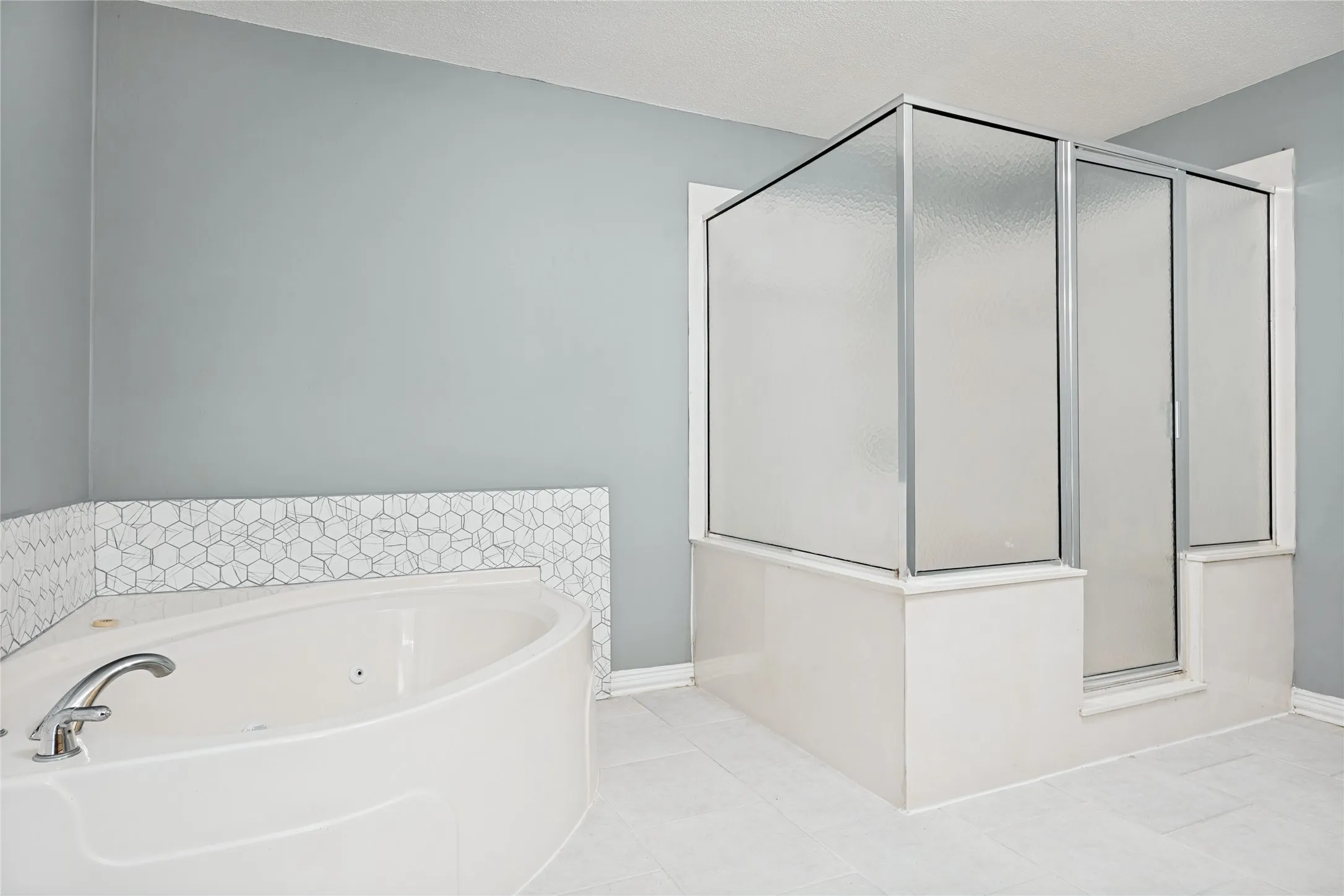 Corner tub, glass-enclosed shower, polished chrome fixtures, hexagonal tile accent, and light-toned floor tile