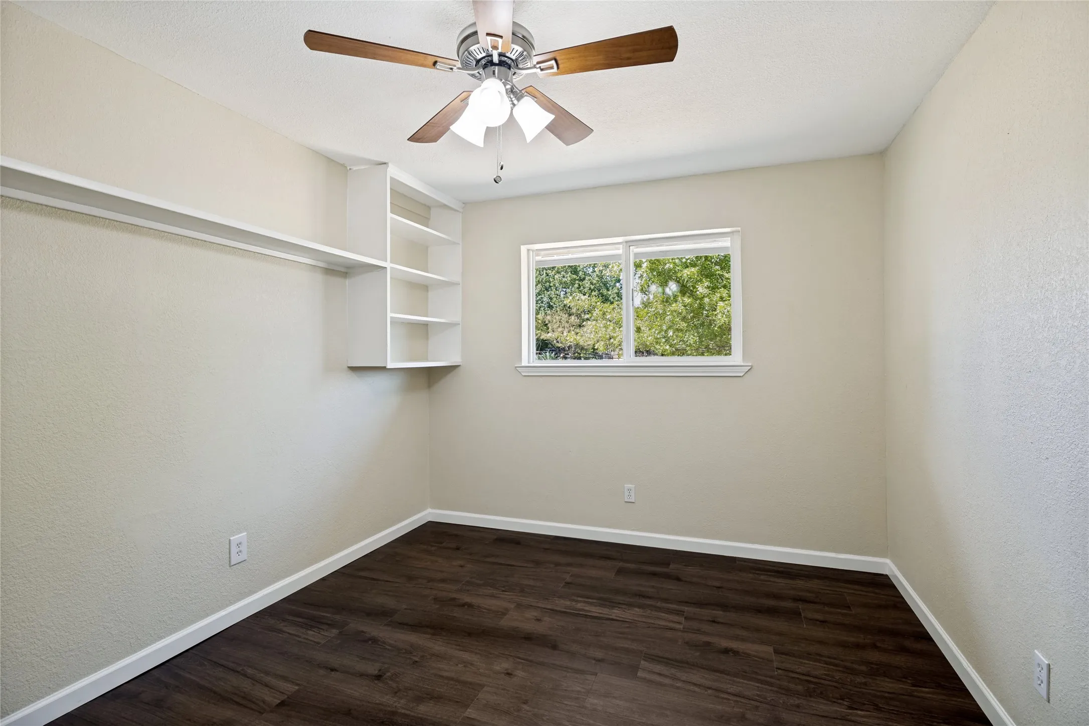 Wood-finish flooring, built-in shelving, white trim, recessed window, and a ceiling fan with integrated lighting