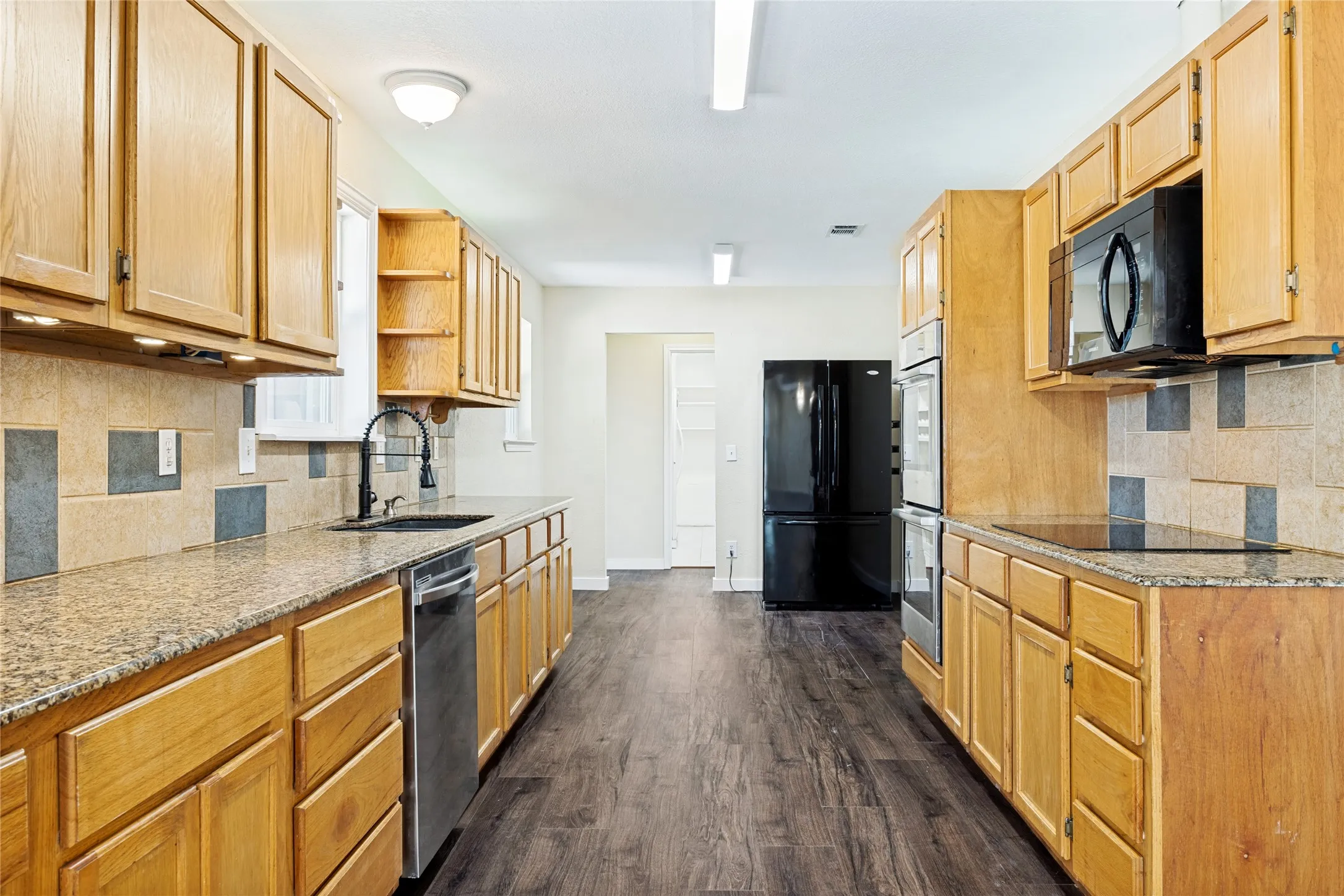 Kitchen featuring wood-finish flooring, light wood cabinetry, stone-finish countertops, a tile backsplash, and a built-in oven and microwave