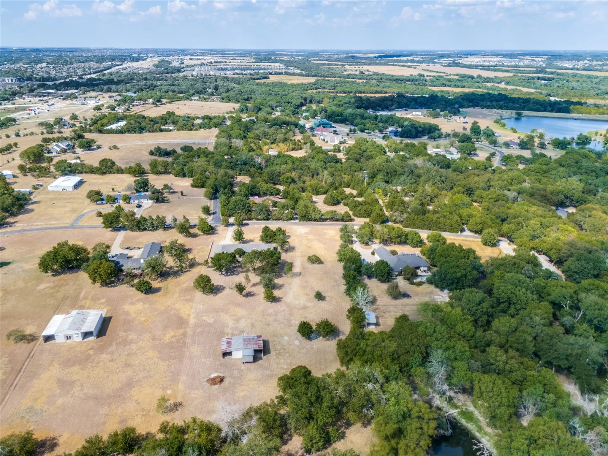 Expansive property featuring multiple structures, mature trees, and a distant body of water