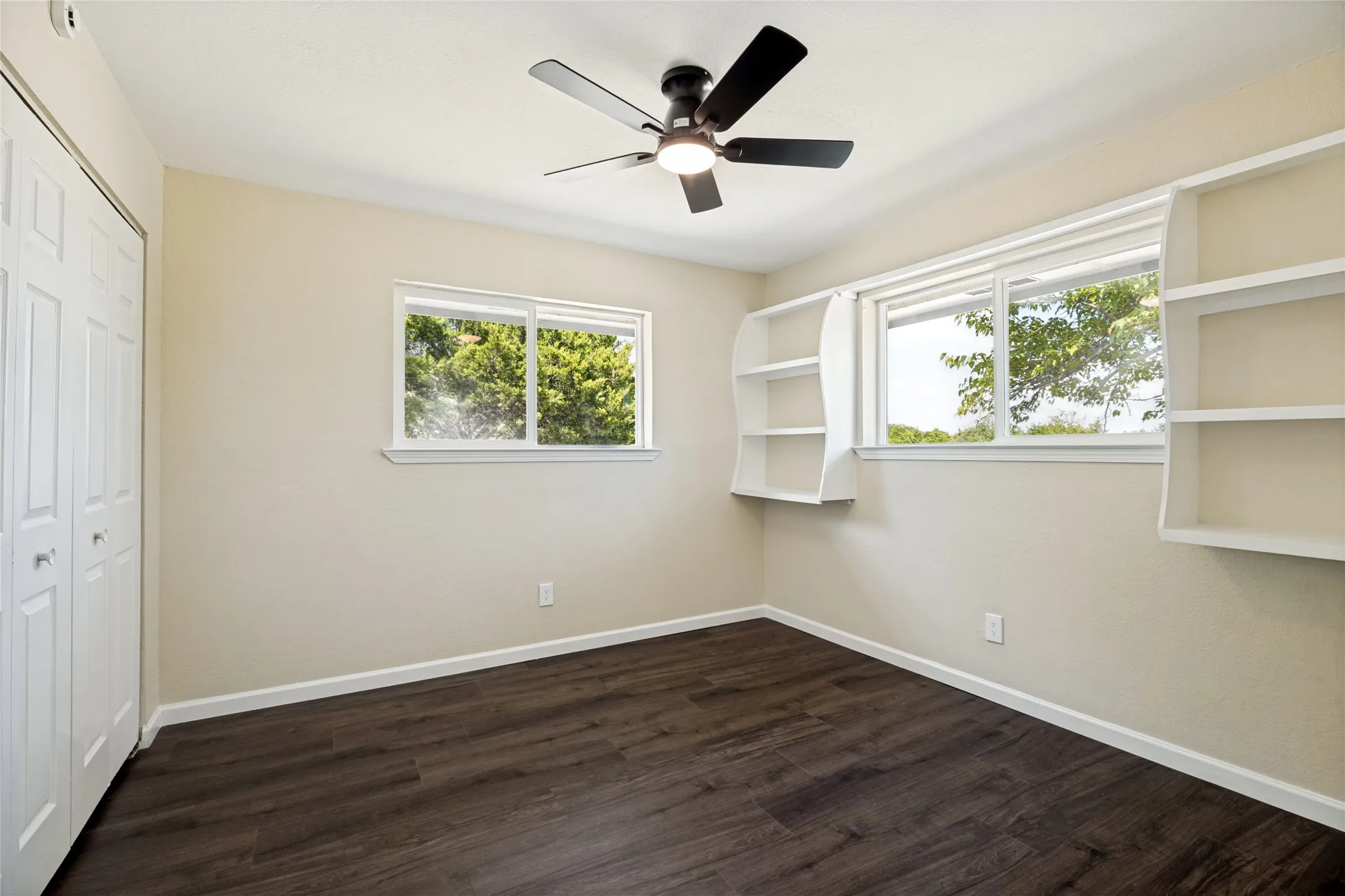 Wood-finish flooring, two large windows, built-in shelving, ceiling fan with light, and bi-fold closet doors