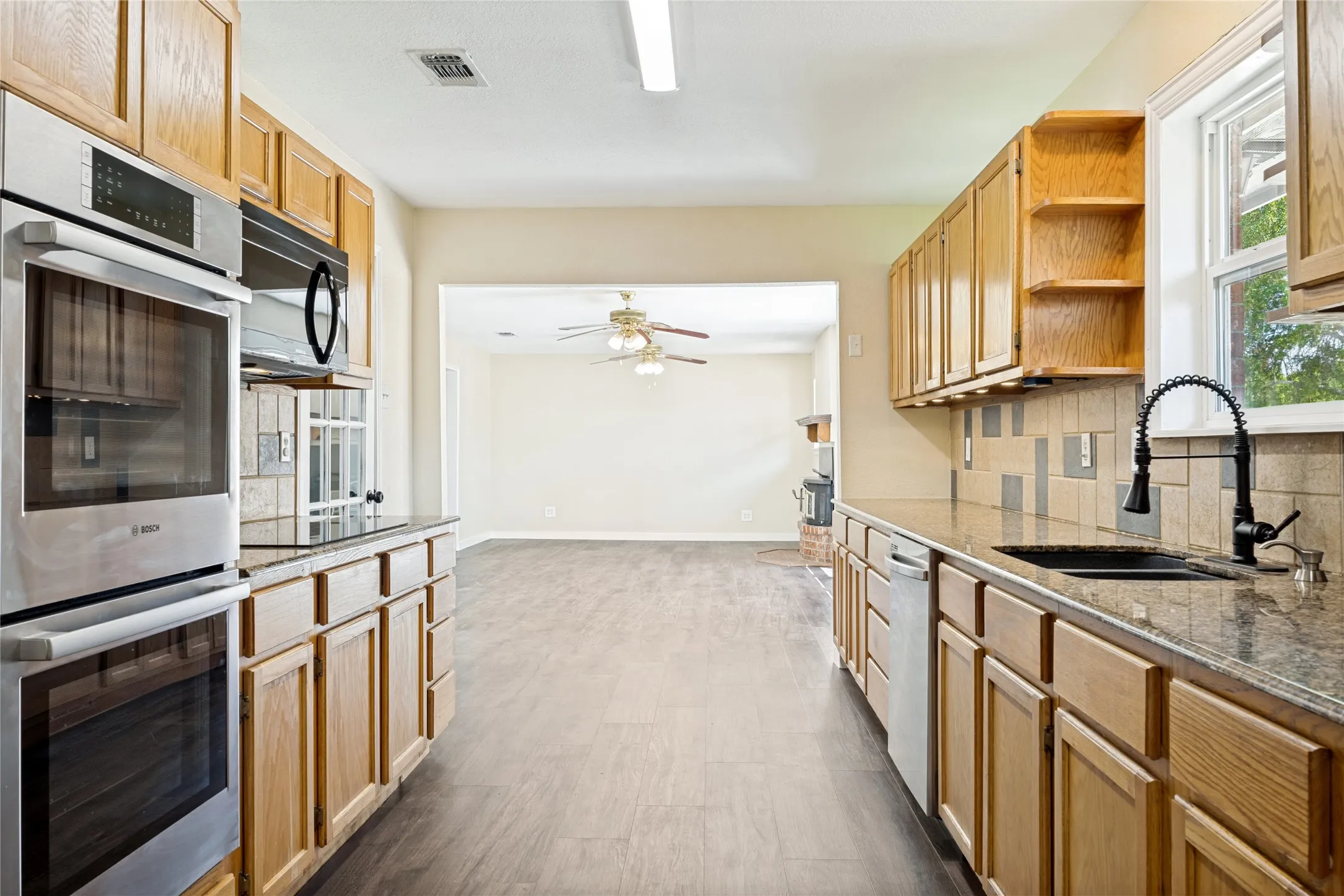 Kitchen featuring wood cabinetry, integrated double ovens, a contemporary black faucet, and stone countertops