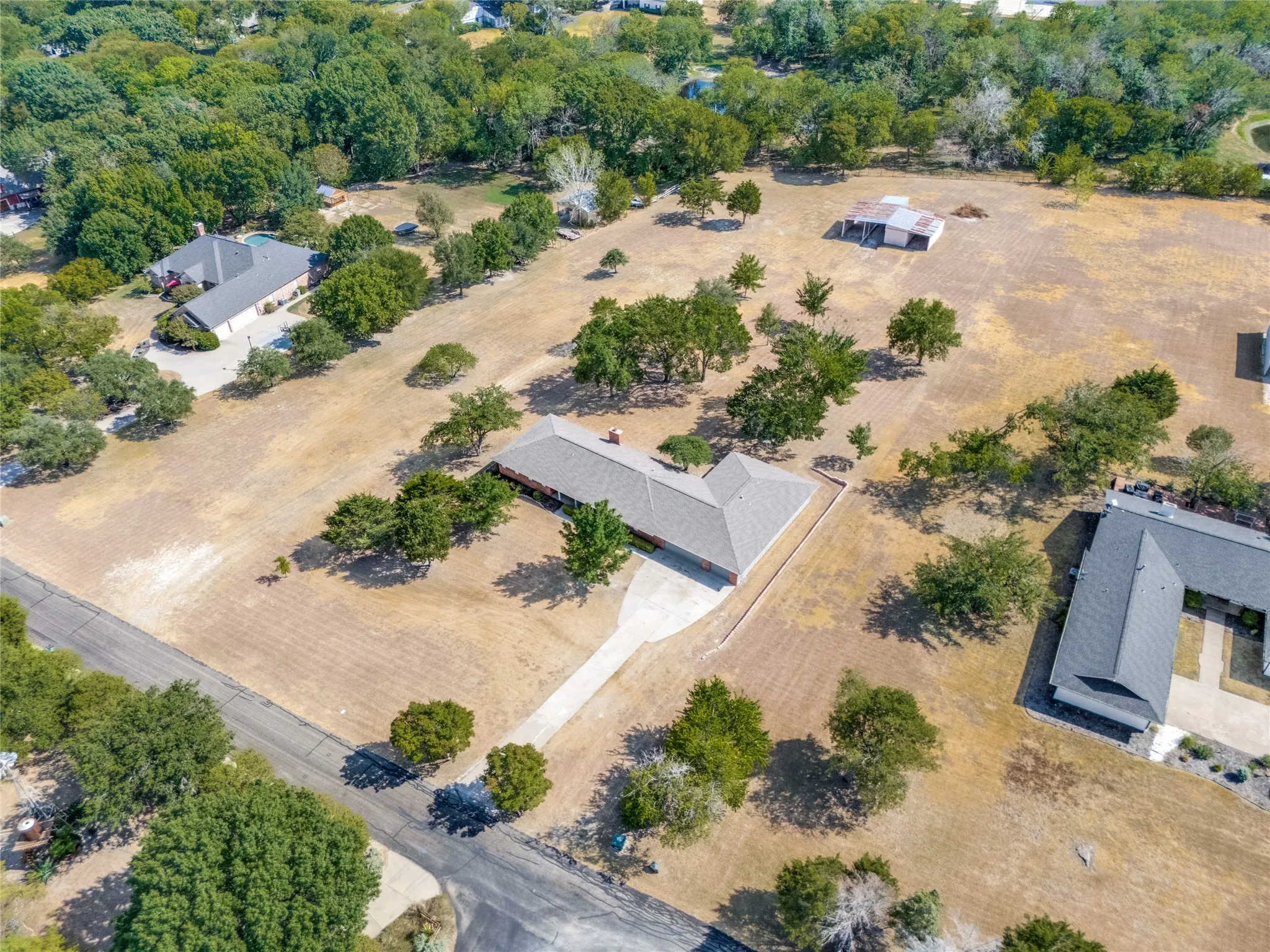 Expansive property featuring a single-story residence, a lengthy paved driveway, and mature landscaping