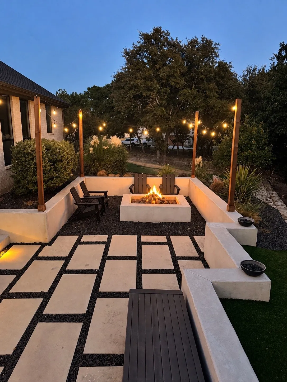 Expansive outdoor patio featuring large-format paver stones, a built-in fire pit, string lighting, decorative gravel, and integrated seating