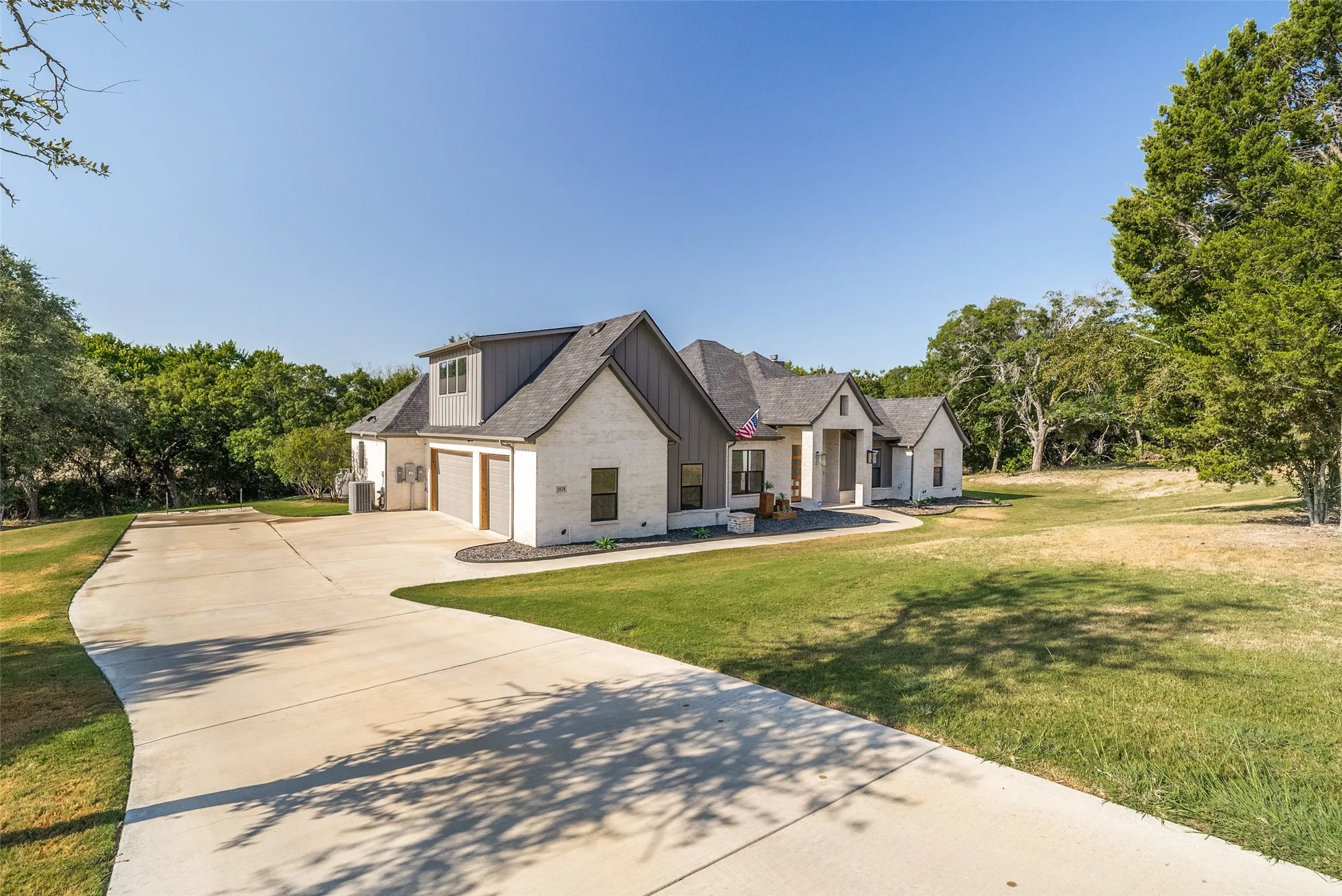 Exterior with white brick and board and batten siding, dark shingle roof, attached garage, and concrete driveway
