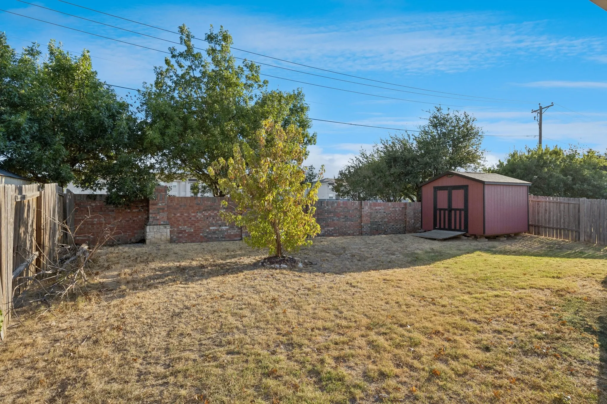 Expansive backyard featuring a privacy fence, mature trees, and a storage shed