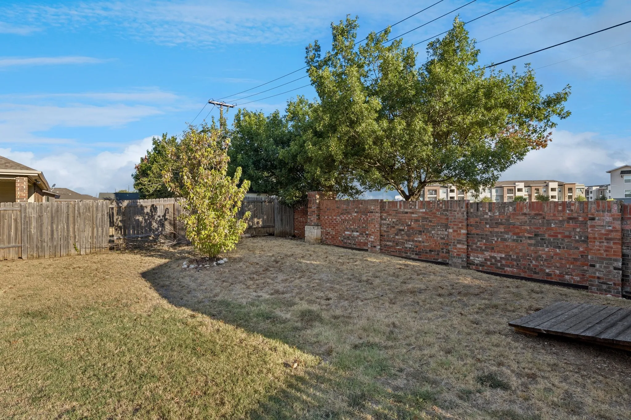 Fenced backyard featuring a brick privacy wall, wood fencing, and established trees