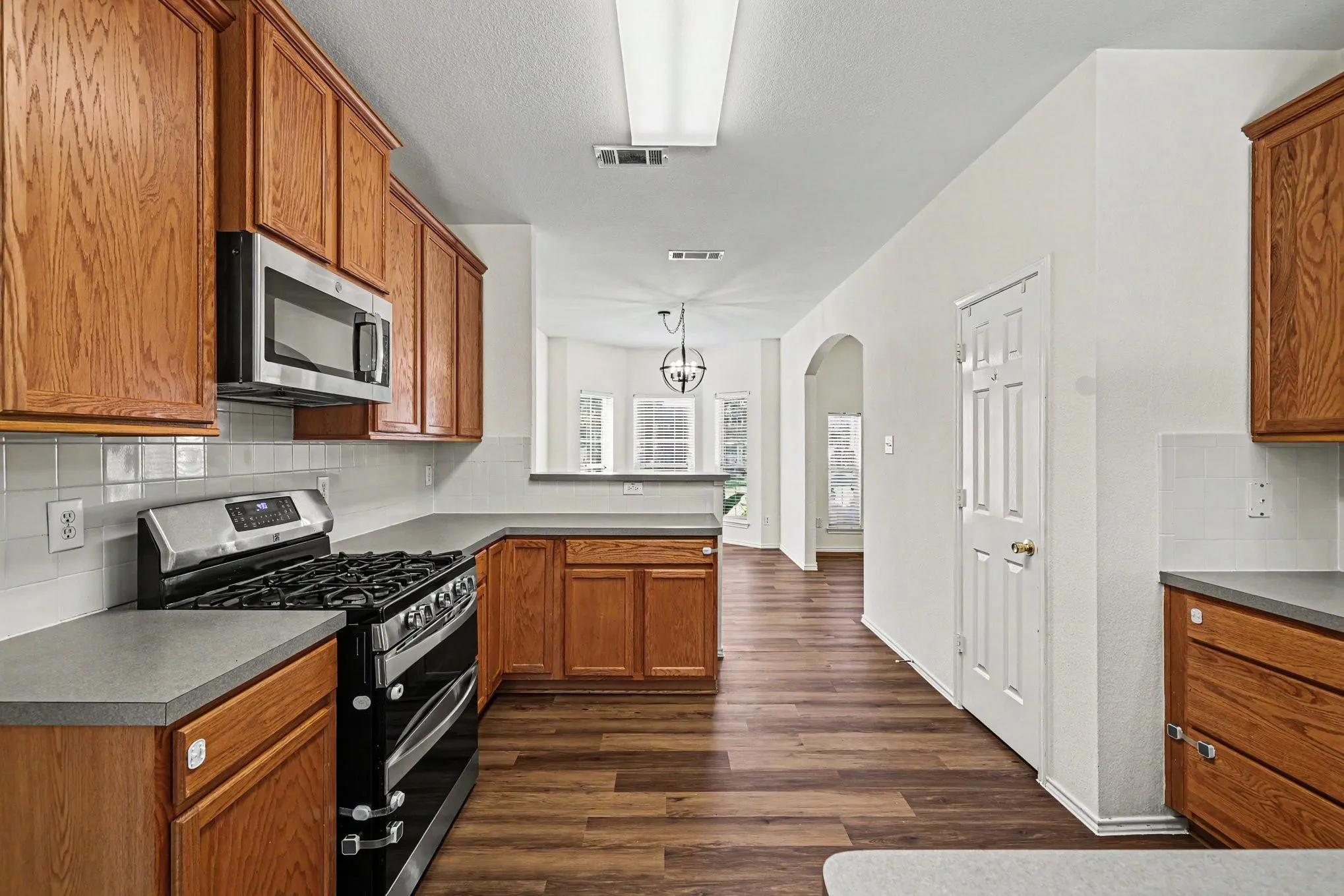 Kitchen featuring wood-finish flooring, wood cabinetry, stainless steel appliances, and a tile backsplash