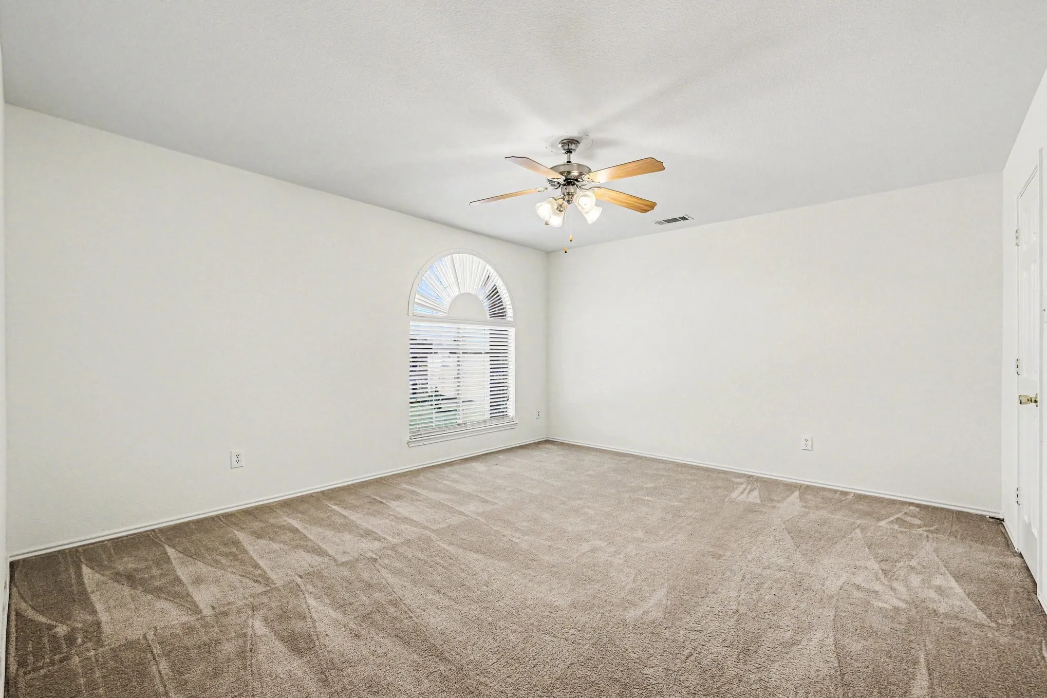 Neutral tone wall finishes, arched window with horizontal blinds, ceiling fan with integrated lighting, and carpet flooring