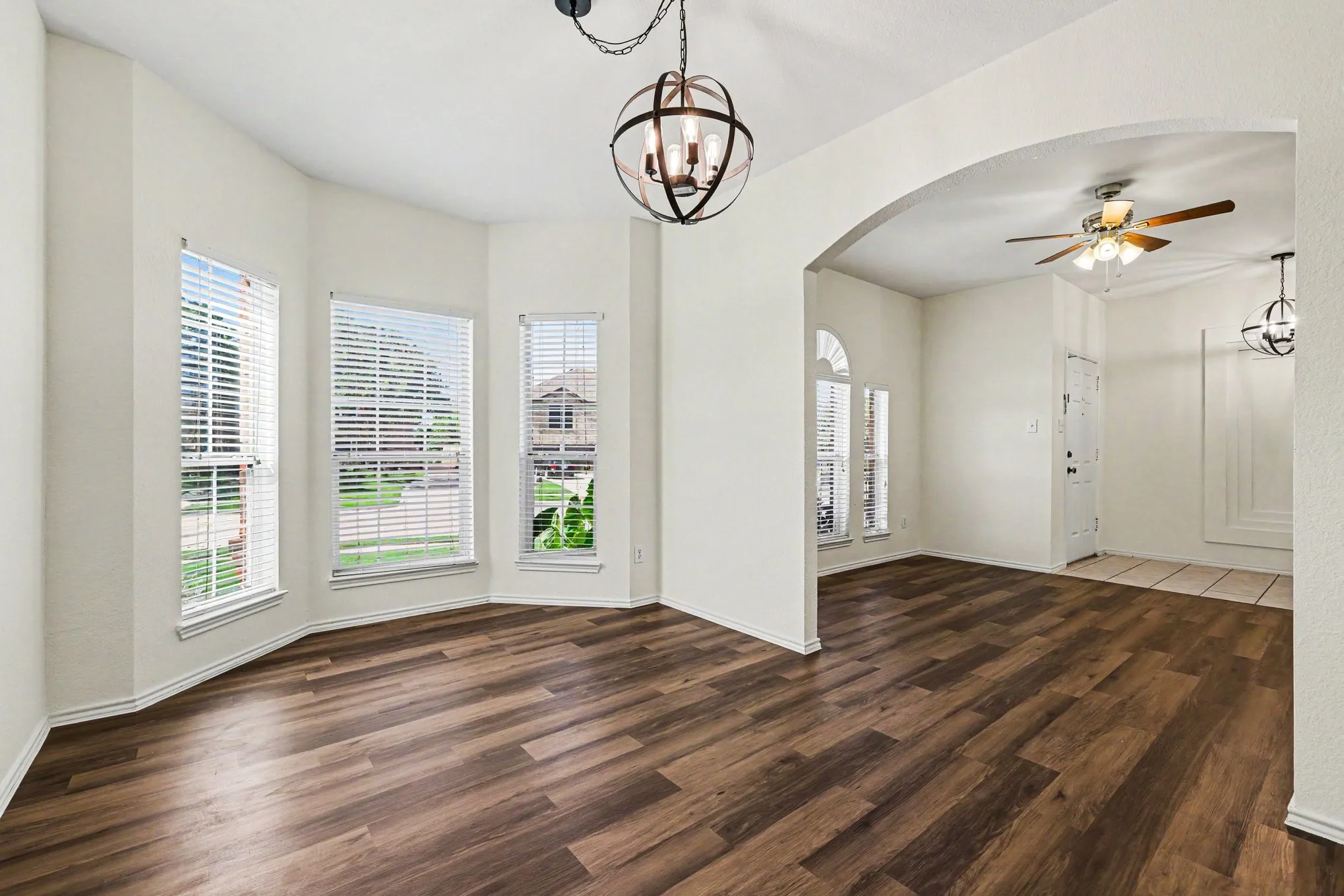 Bay window with multiple panes, wood-finish flooring, arched entryway, and orb pendant lighting