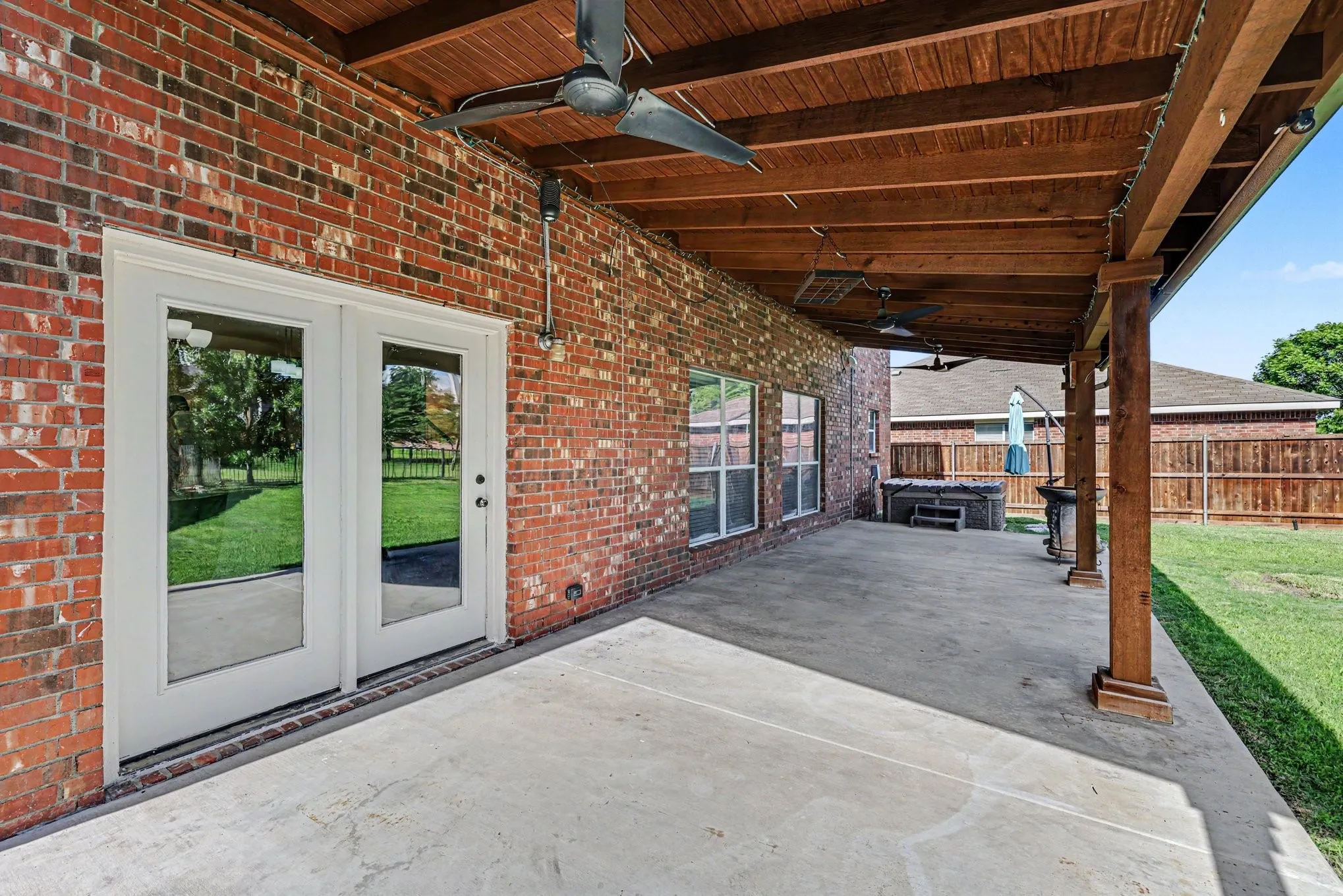 Brick exterior with a covered patio featuring a wood-finish ceiling, concrete flooring, and ceiling fans