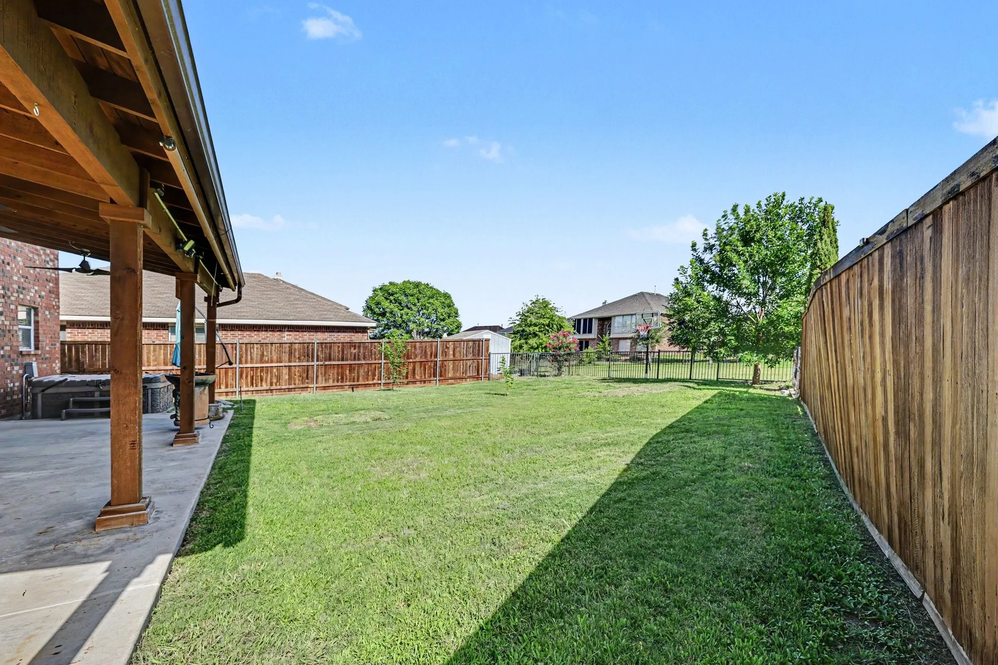 Expansive backyard featuring a large concrete patio, a covered wooden pergola, a full wood privacy fence, and mature trees