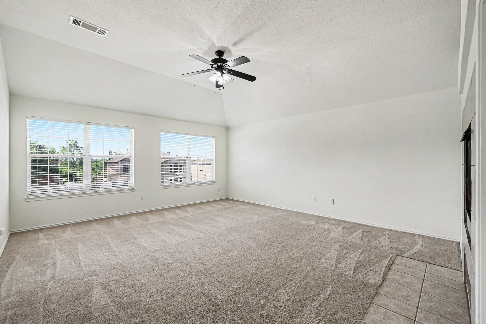 Vaulted ceiling with a ceiling fan, two windows, wall-to-wall carpeting, and a tiled hearth