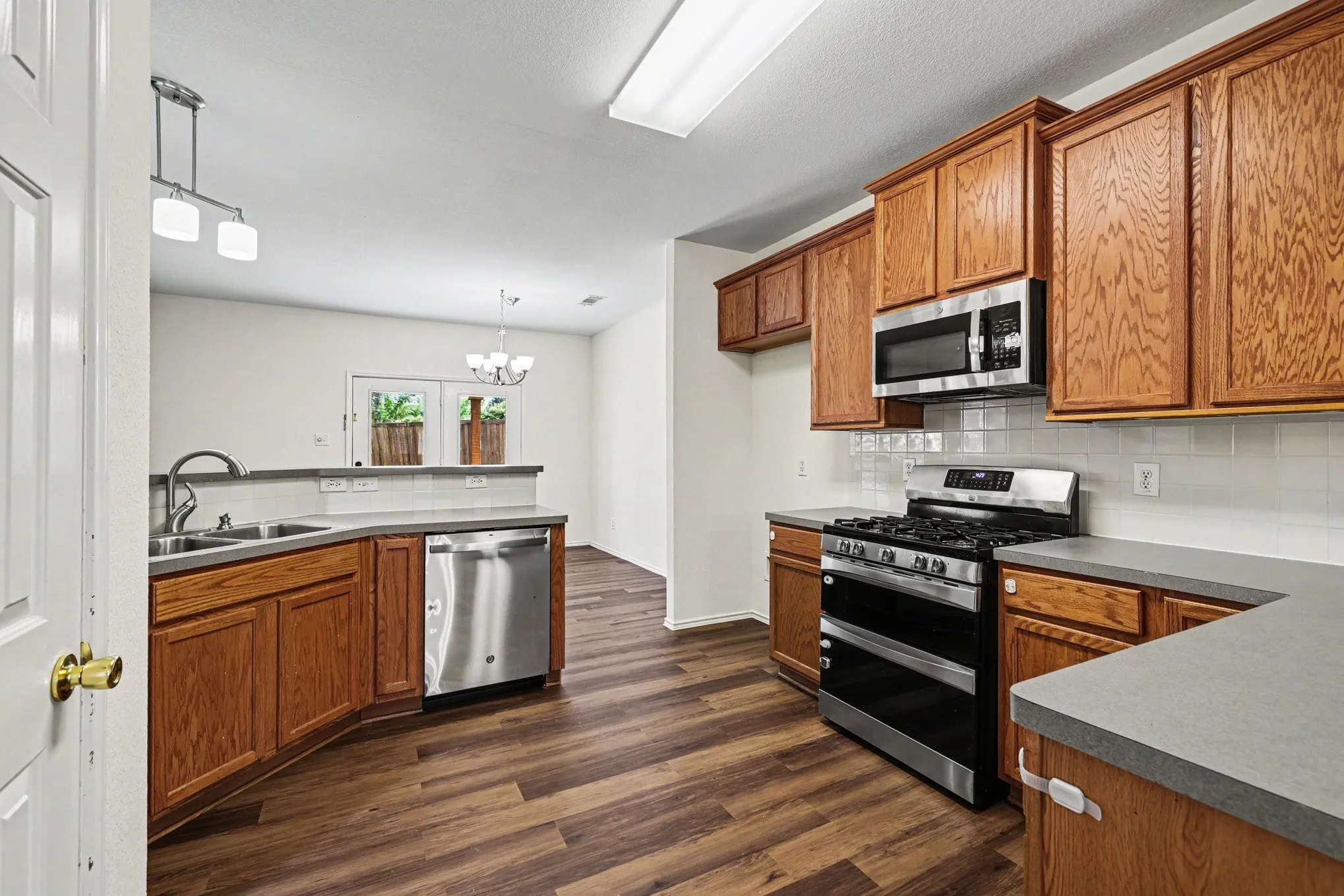 Kitchen featuring wood-finish flooring, stainless steel appliances, wood cabinetry, light countertops, and a white subway tile backsplash