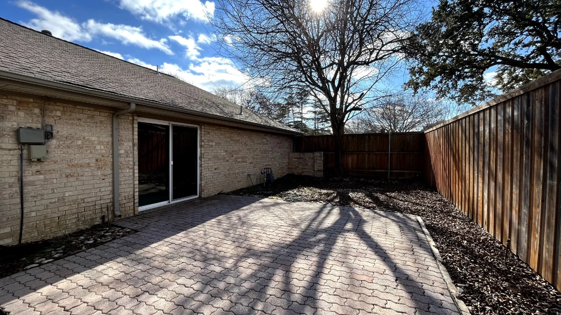 Brick exterior with a paved patio, sliding glass door, and wood privacy fencing