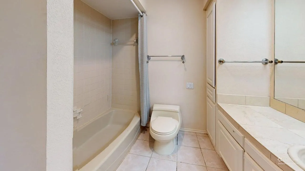 Tiled flooring with a built-in bathtub and shower, complemented by a white vanity with cabinet storage and a mirror