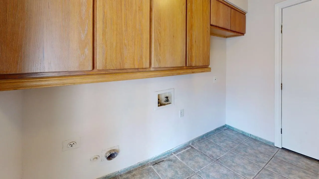 Upper wood-finish cabinetry, white walls, and tiled flooring