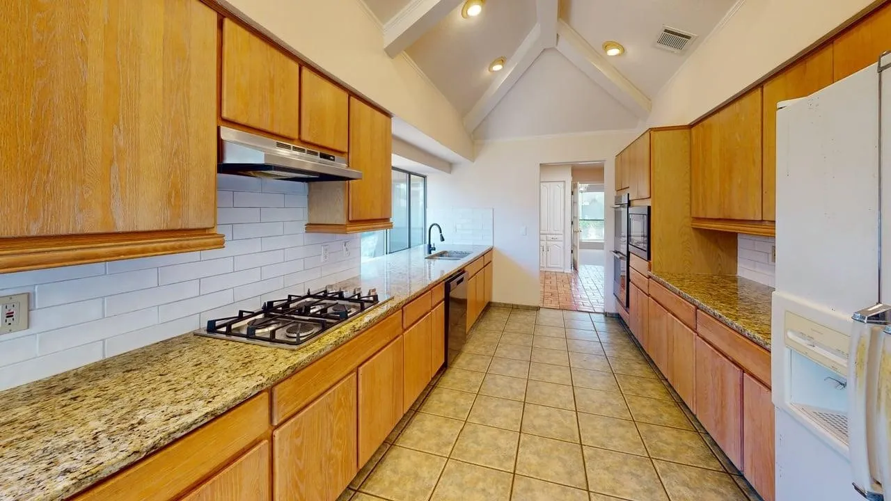 Kitchen featuring vaulted ceilings with exposed beams, recessed lighting, wood cabinetry, granite countertops, and tile flooring