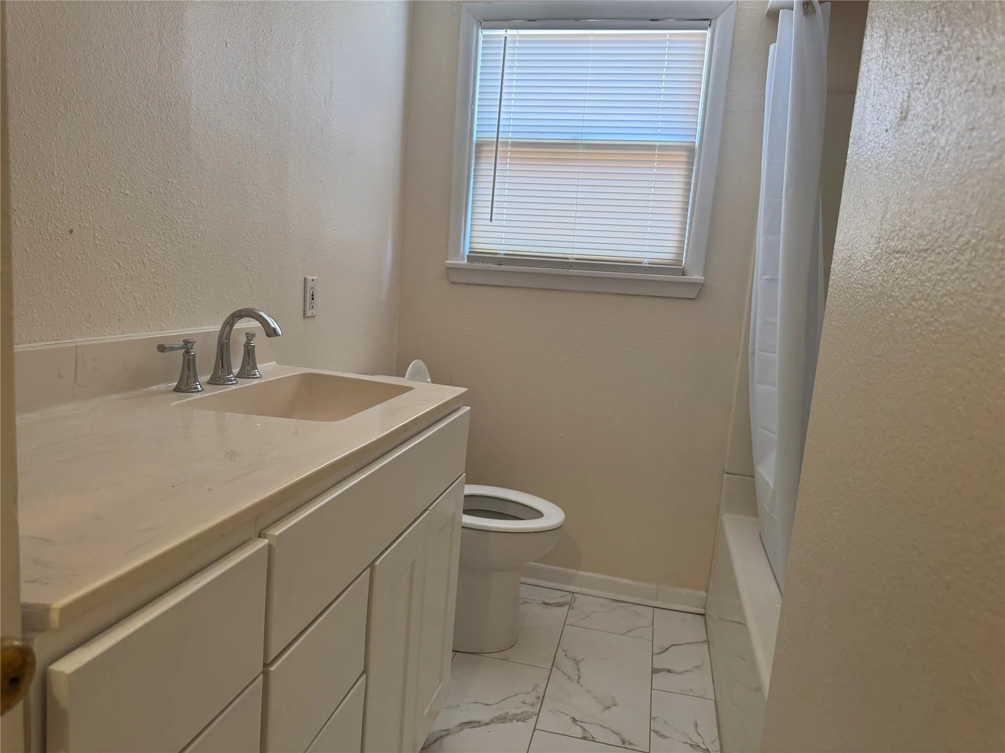 Integrated vanity with undermount sink, dual-handle faucet, white cabinetry, tiled flooring, and a bathtub with a shower