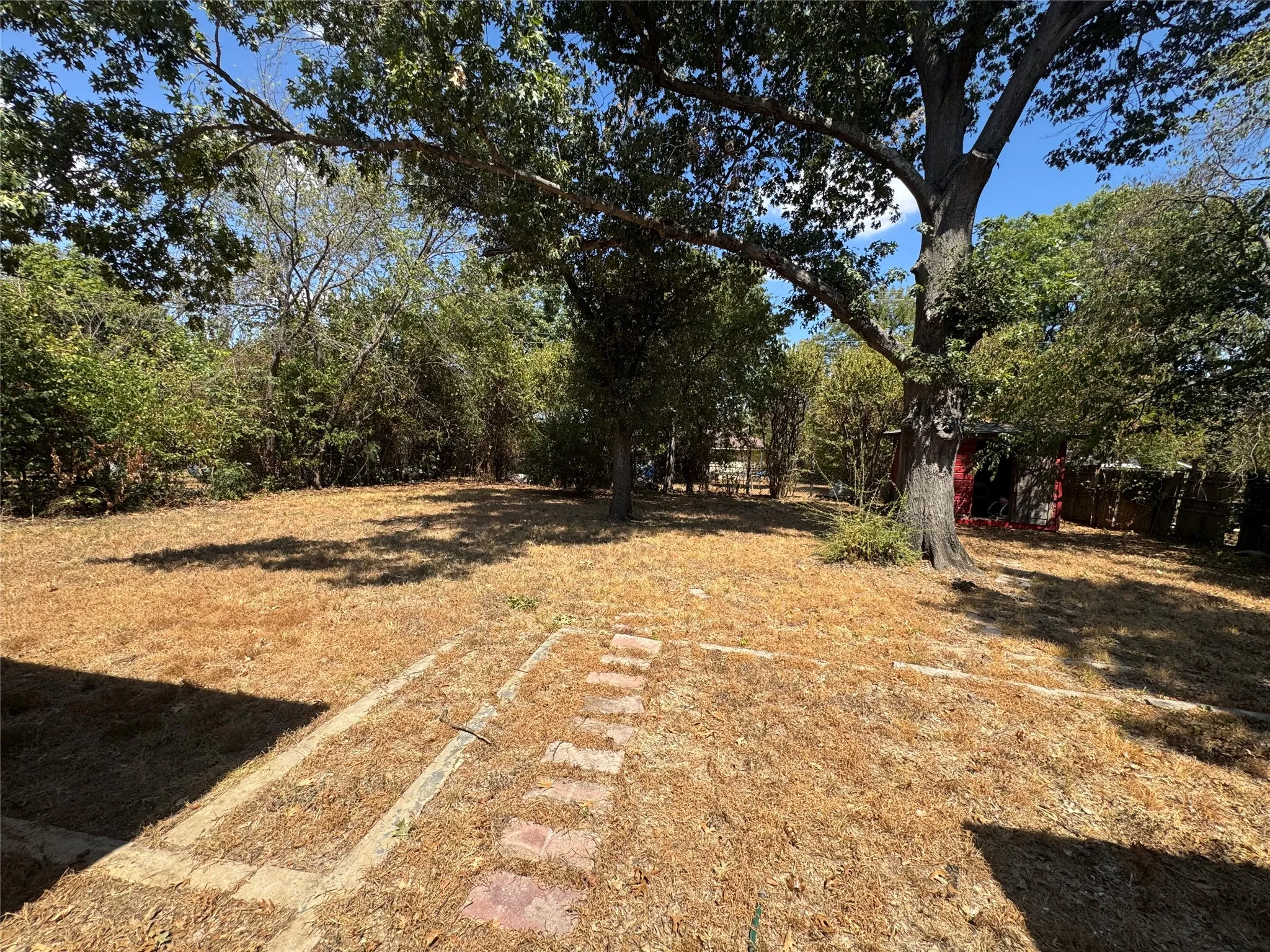 Expansive yard featuring mature trees, a stepping stone path, and perimeter shrubbery