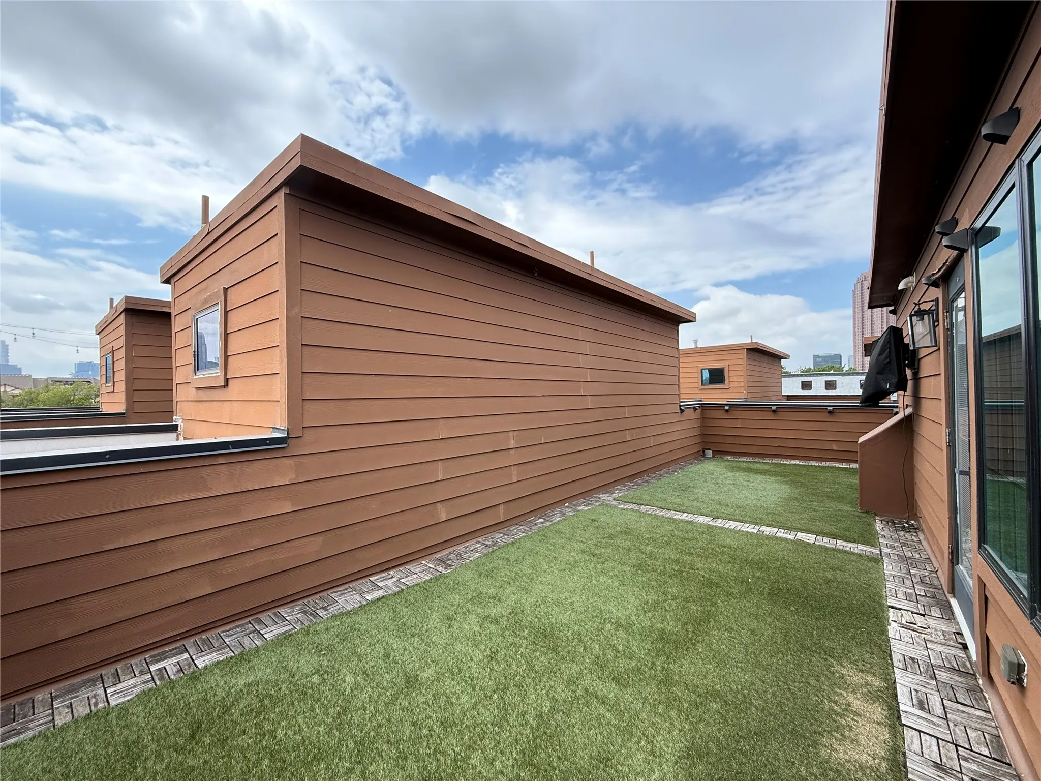 Rooftop deck featuring artificial turf, decorative paver borders, and privacy fencing