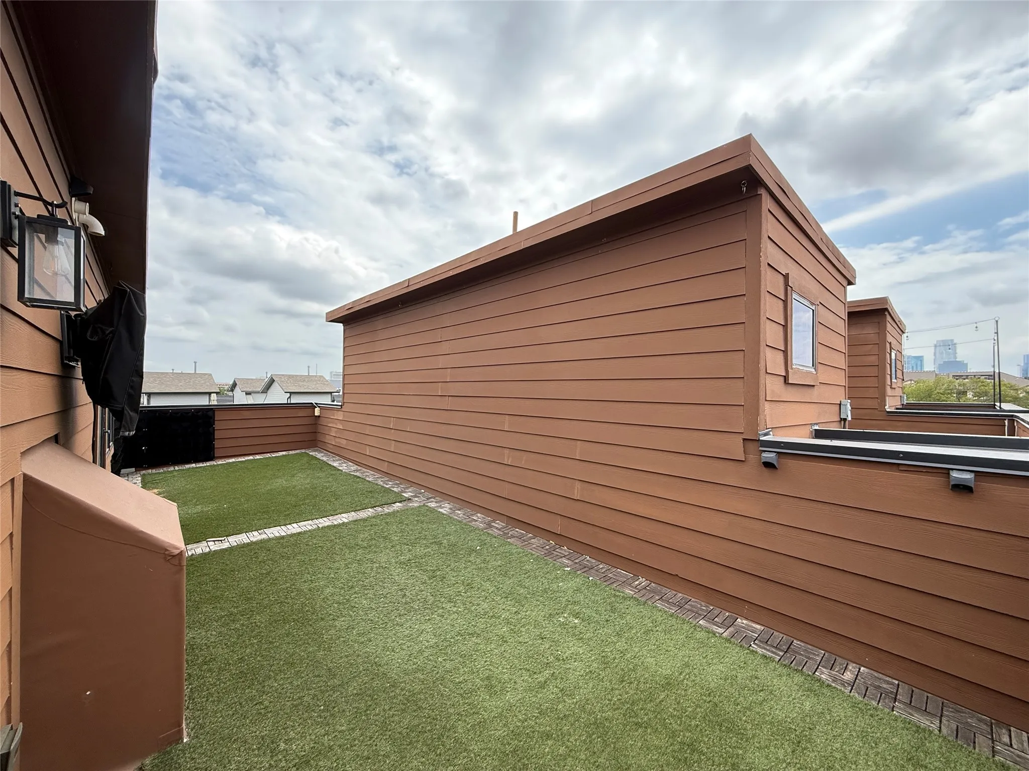 Rooftop terrace featuring artificial turf, brick-lined borders, and horizontal siding
