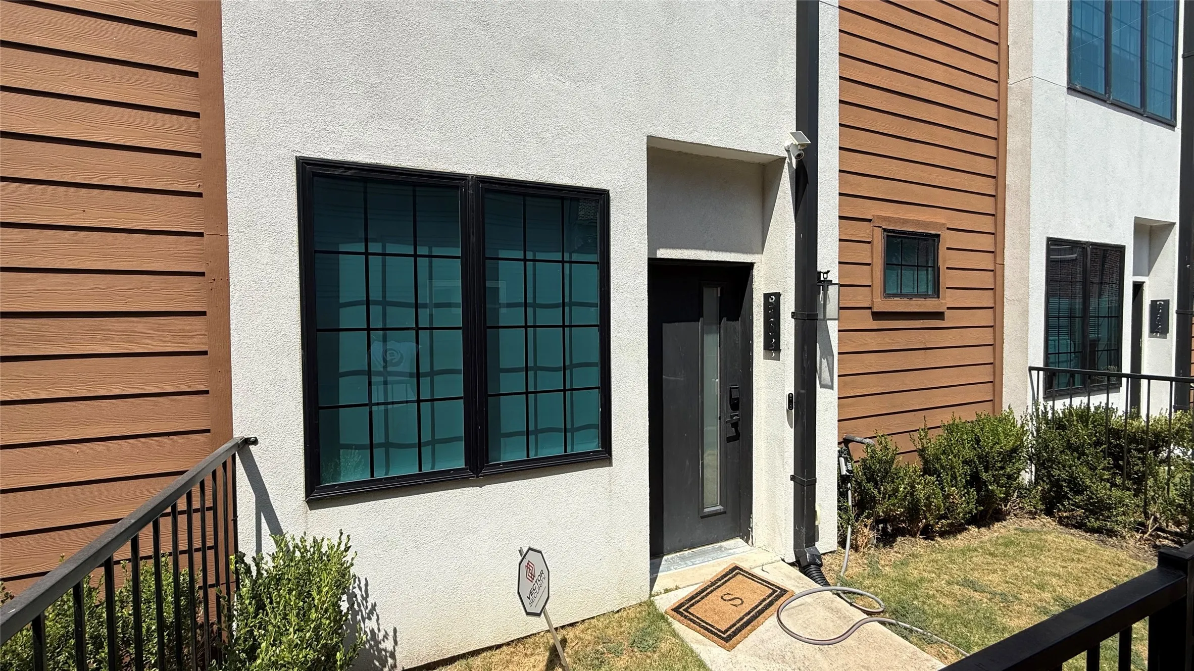 Stucco and horizontal wood-look siding exterior, black-framed windows with grid patterns, dark-toned entry door, and manicured shrubbery