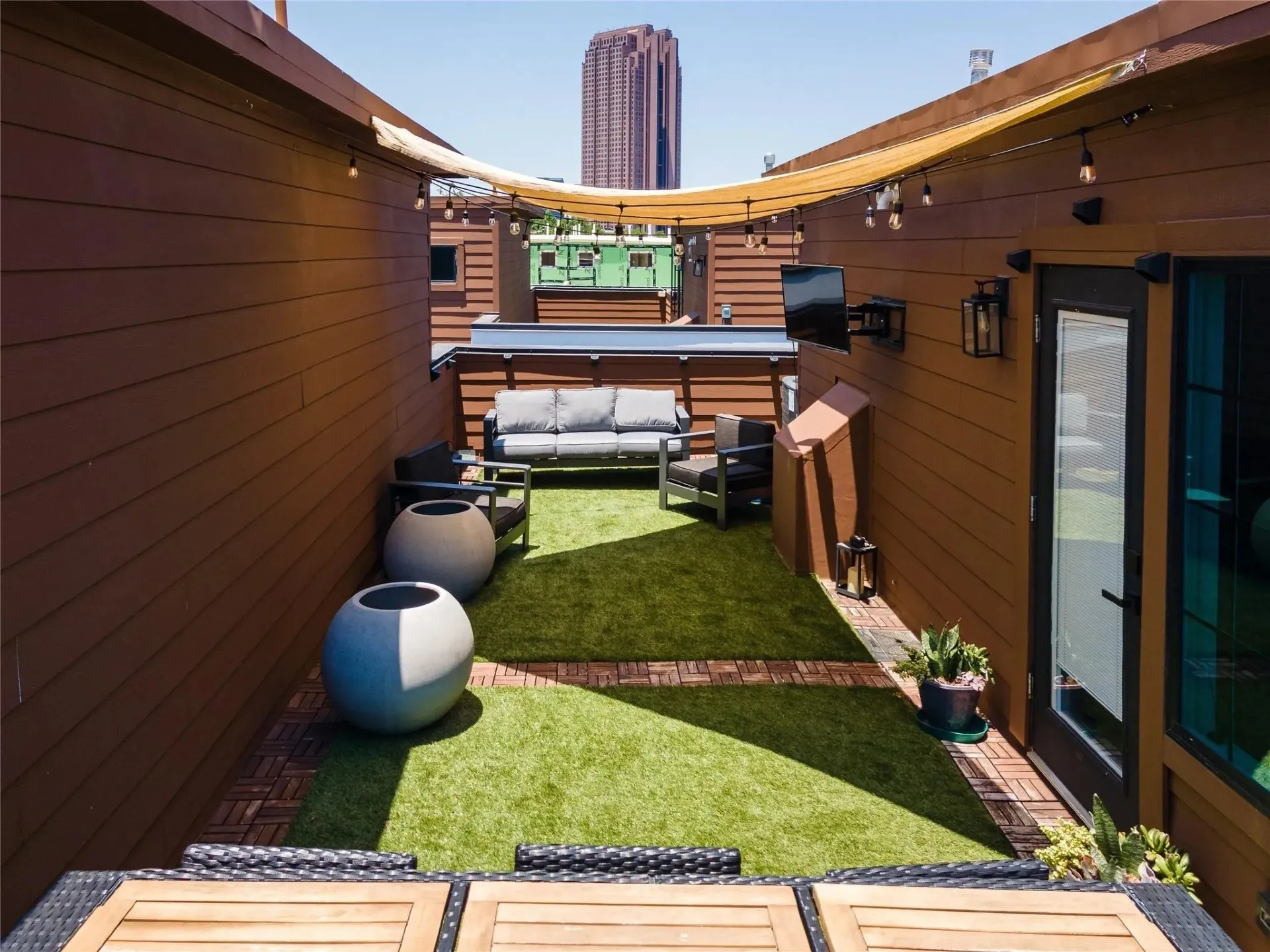 Rooftop patio featuring wood-finish siding, artificial turf, wood tile accents, and string lighting
