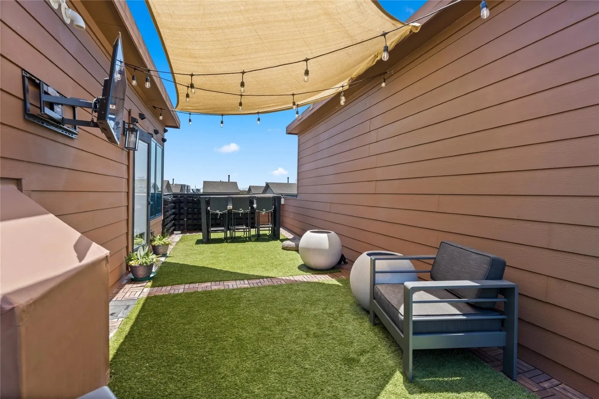 Rooftop deck featuring artificial turf, a sunshade, string lighting, and a built-in outdoor bar