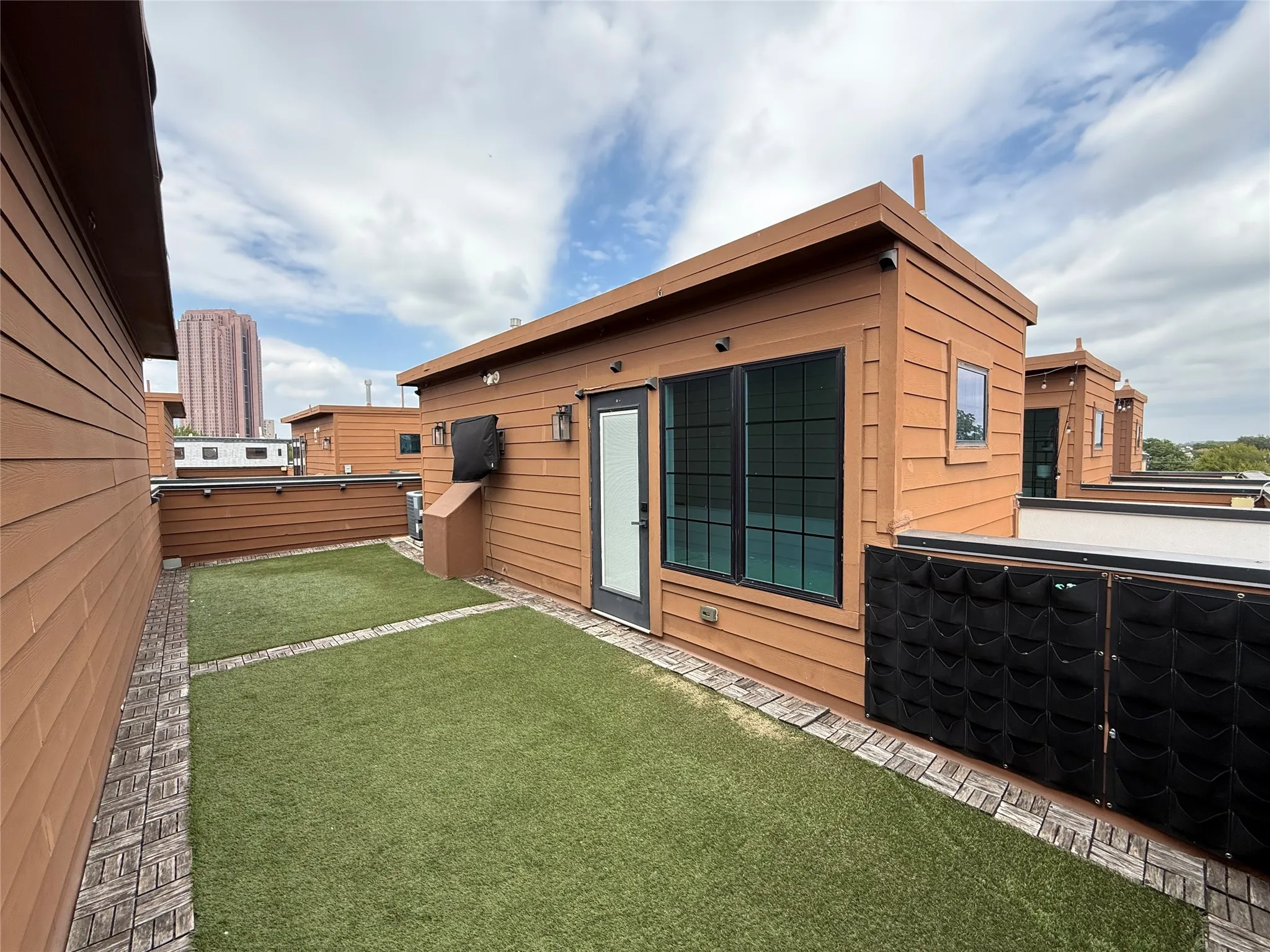 Rooftop terrace with artificial turf, brick-patterned hardscaping, and exterior wood siding