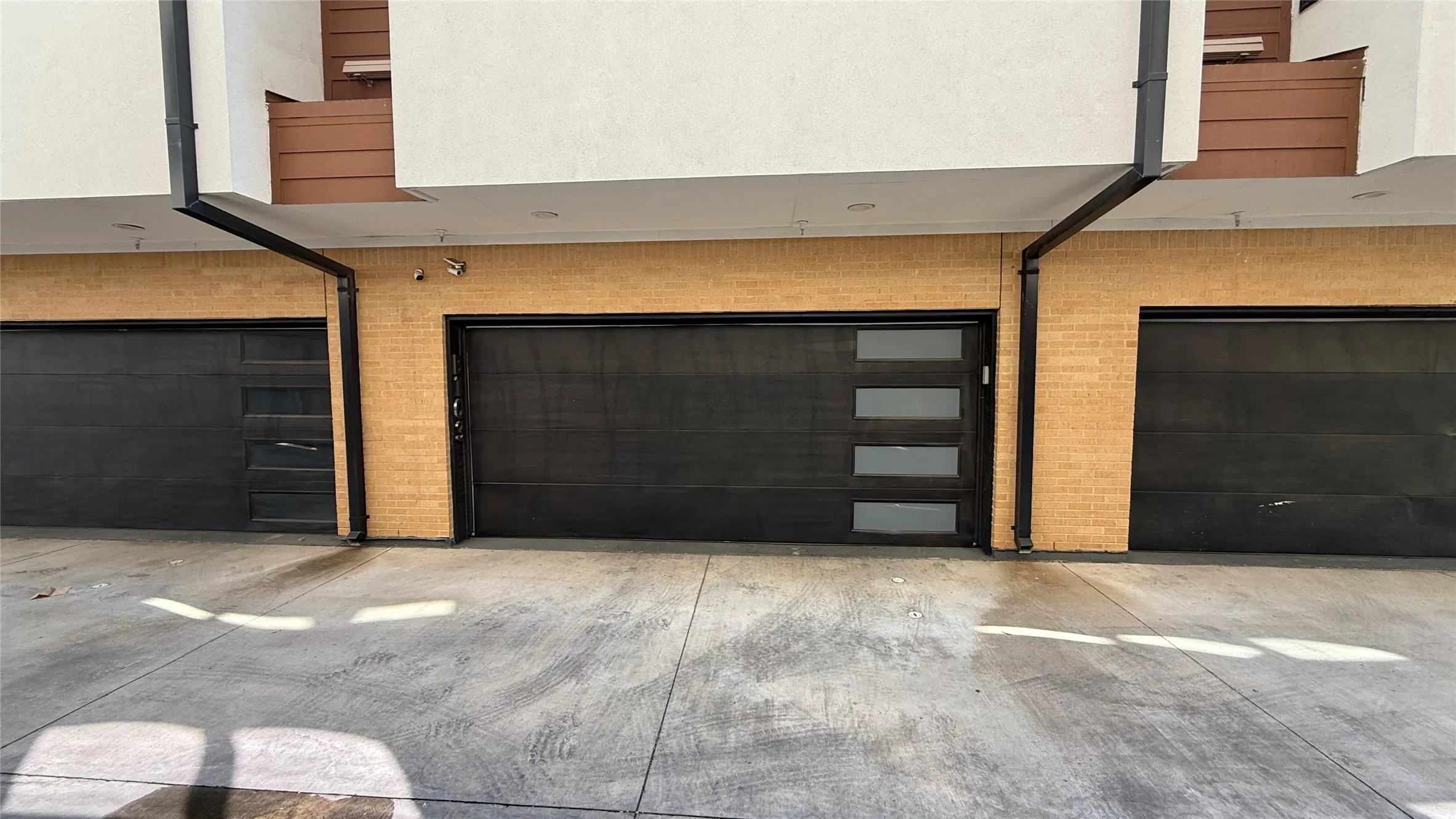 Three modern dark-finish garage doors with one featuring horizontal frosted glass panels