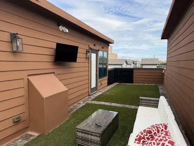 Outdoor patio featuring artificial turf, brick paver accents, and exterior lighting fixtures
