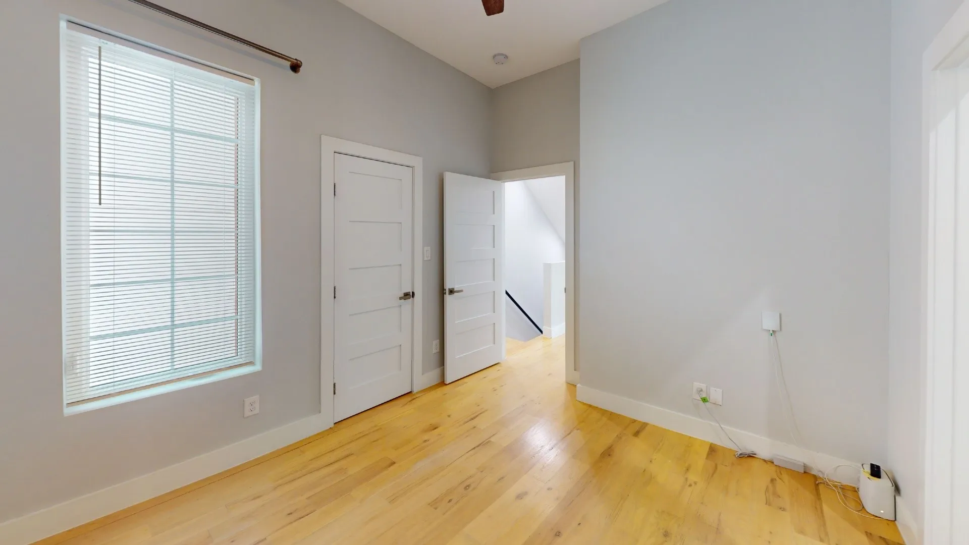 Hardwood flooring, light gray wall finishes, white trim, and a window with blinds