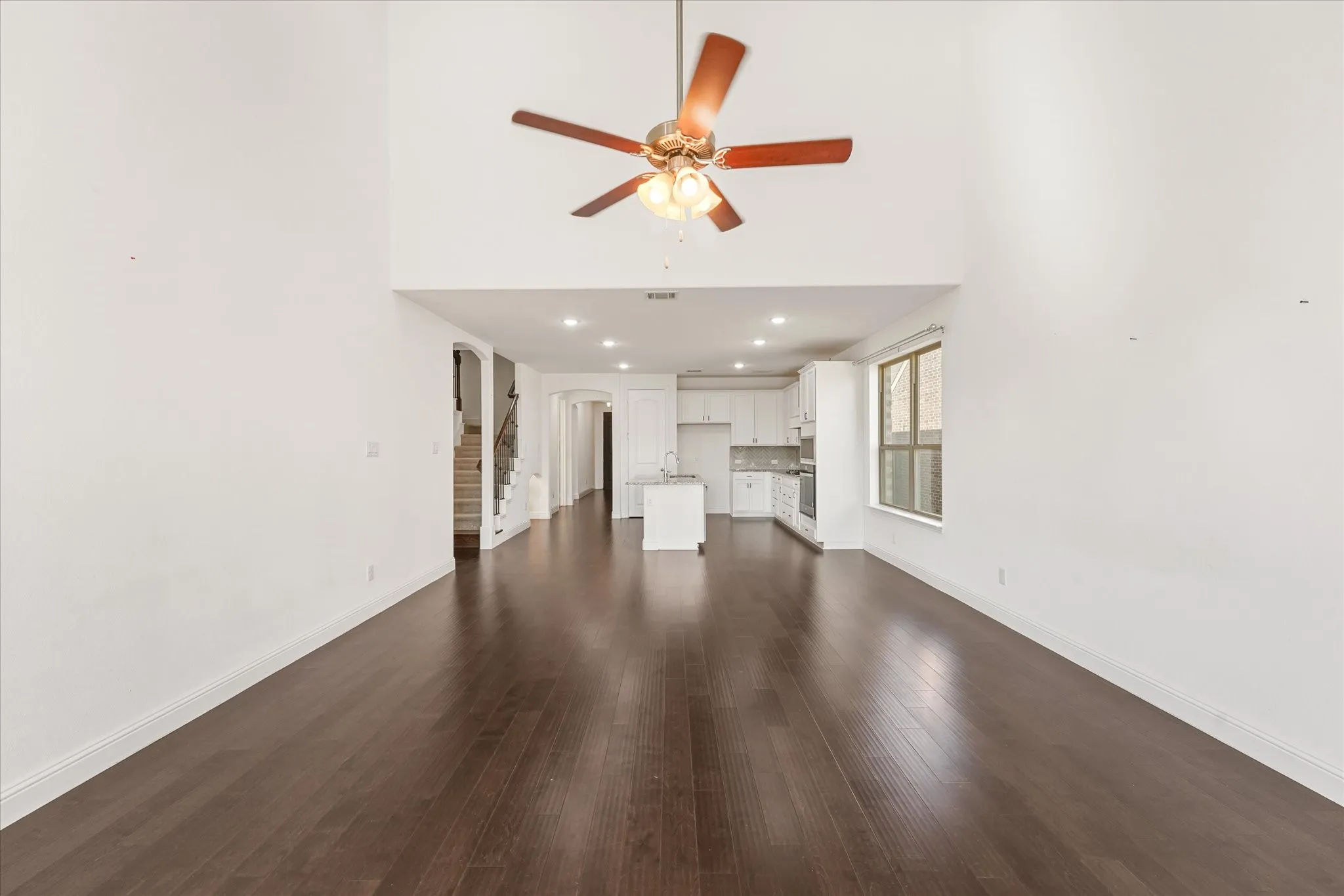 Voluminous ceiling with a ceiling fan, dark wood-finish flooring, recessed lighting, and a modern kitchen with white cabinetry