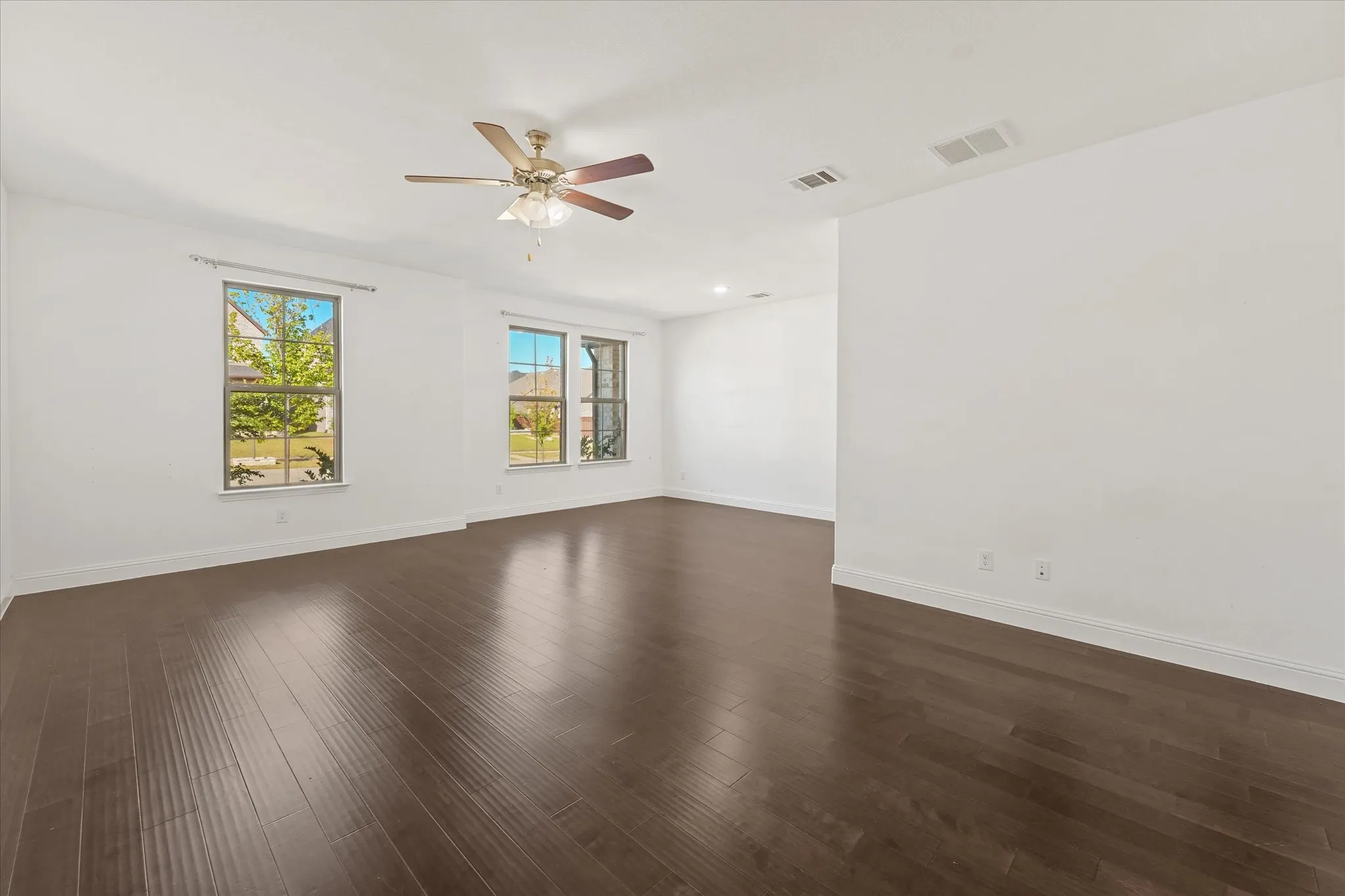 Expansive interior with wood-finish flooring, multiple windows, and a ceiling fan with integrated lighting