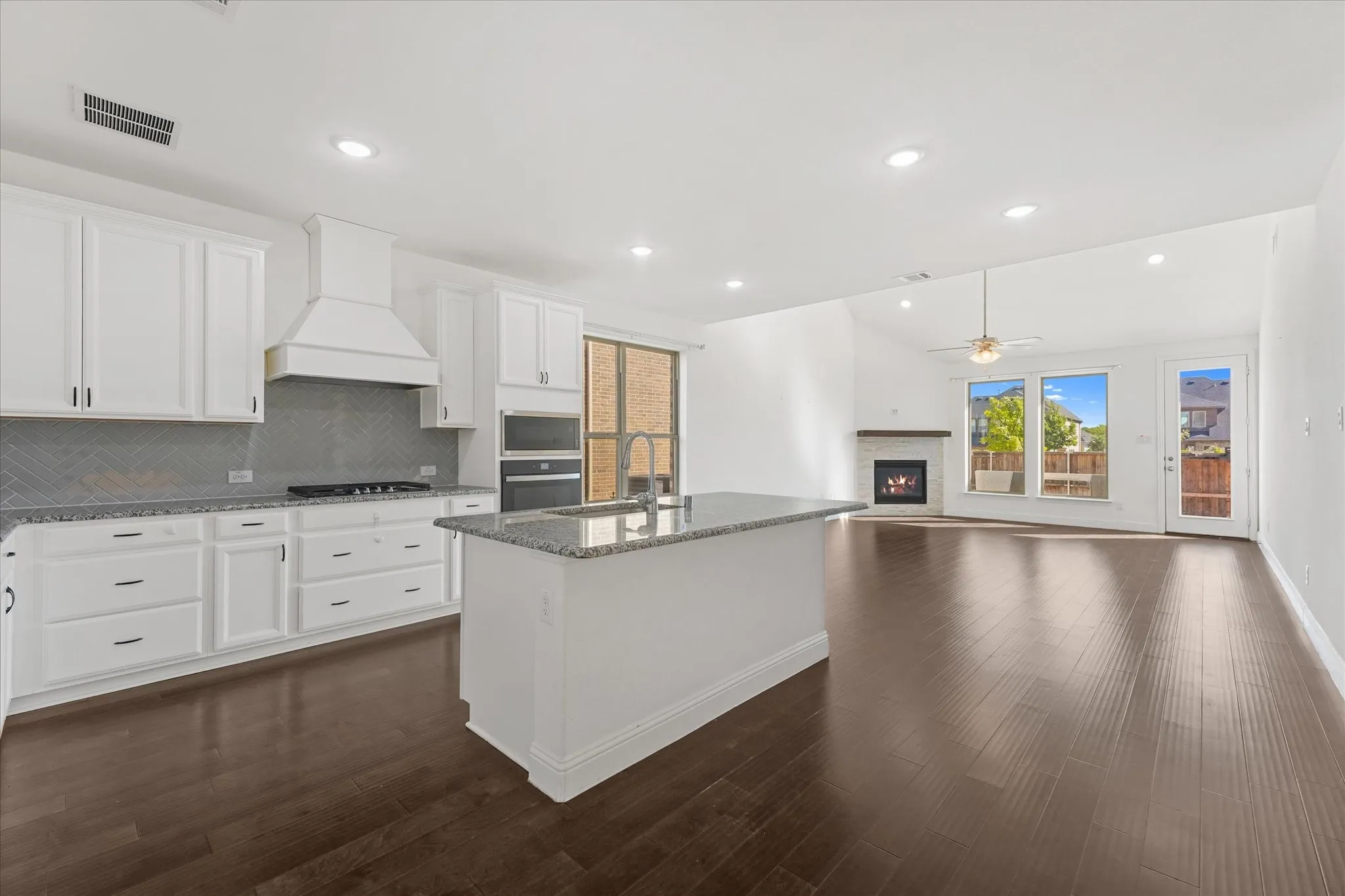 Spacious open-concept living area featuring wood-finish flooring, recessed lighting, and a kitchen island with a stone-finish countertop