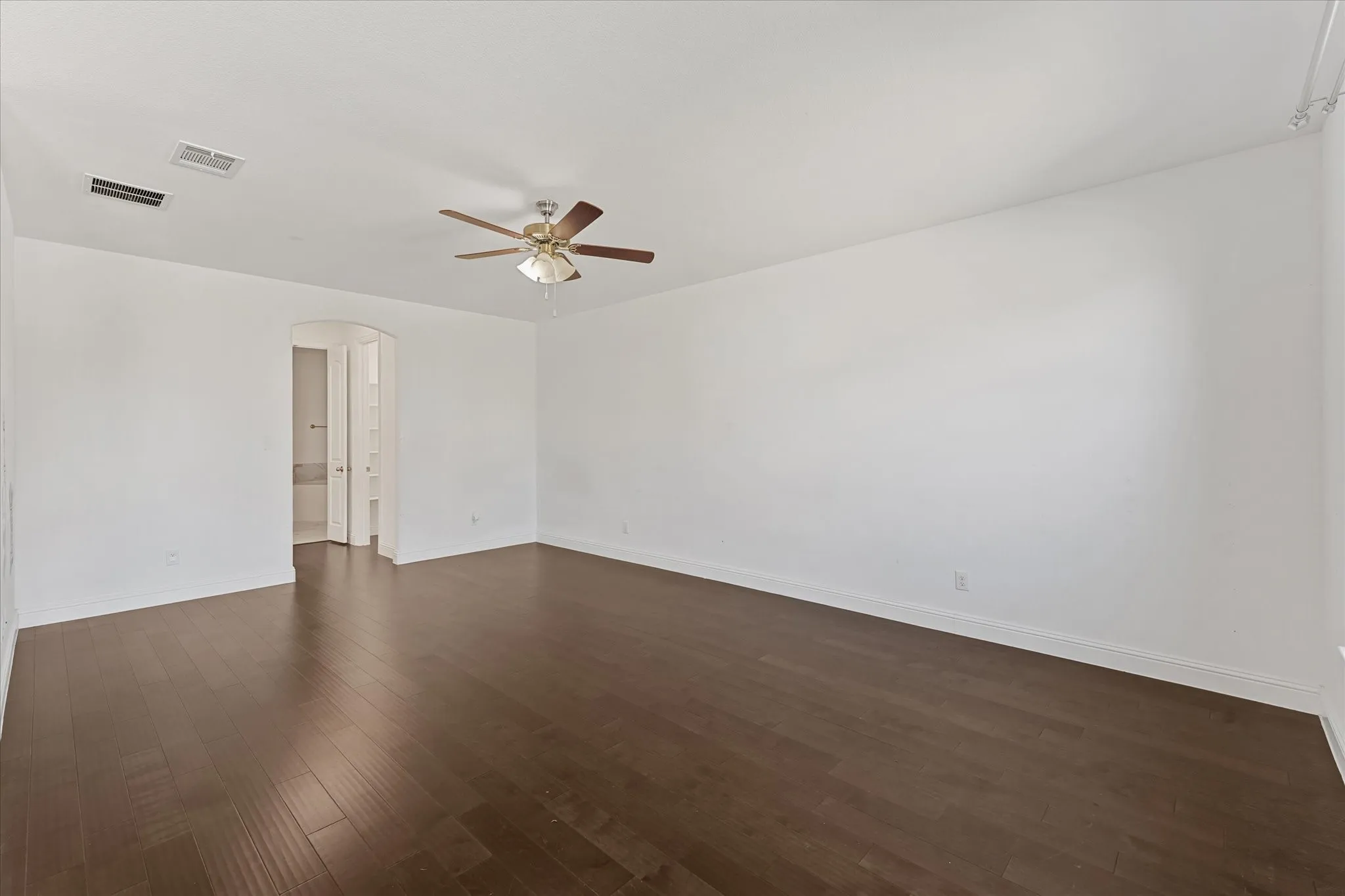 Expansive room featuring wood-finish flooring, a ceiling fan, and an arched doorway