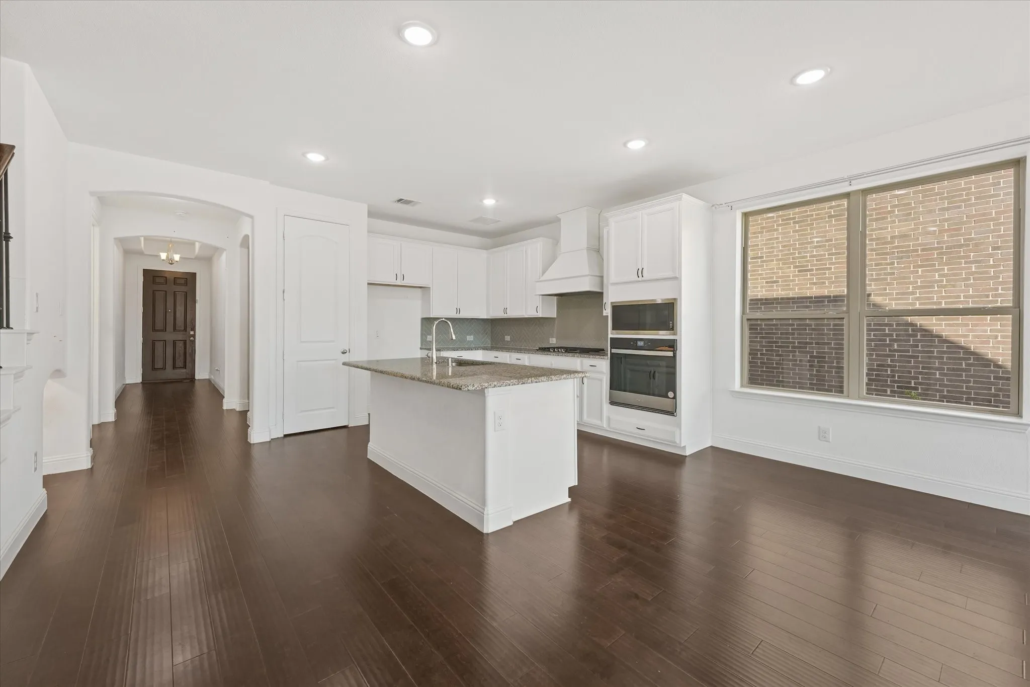 Expansive wood-finish flooring, recessed lighting, white cabinetry, a kitchen island with stone countertops, and a built-in oven and microwave
