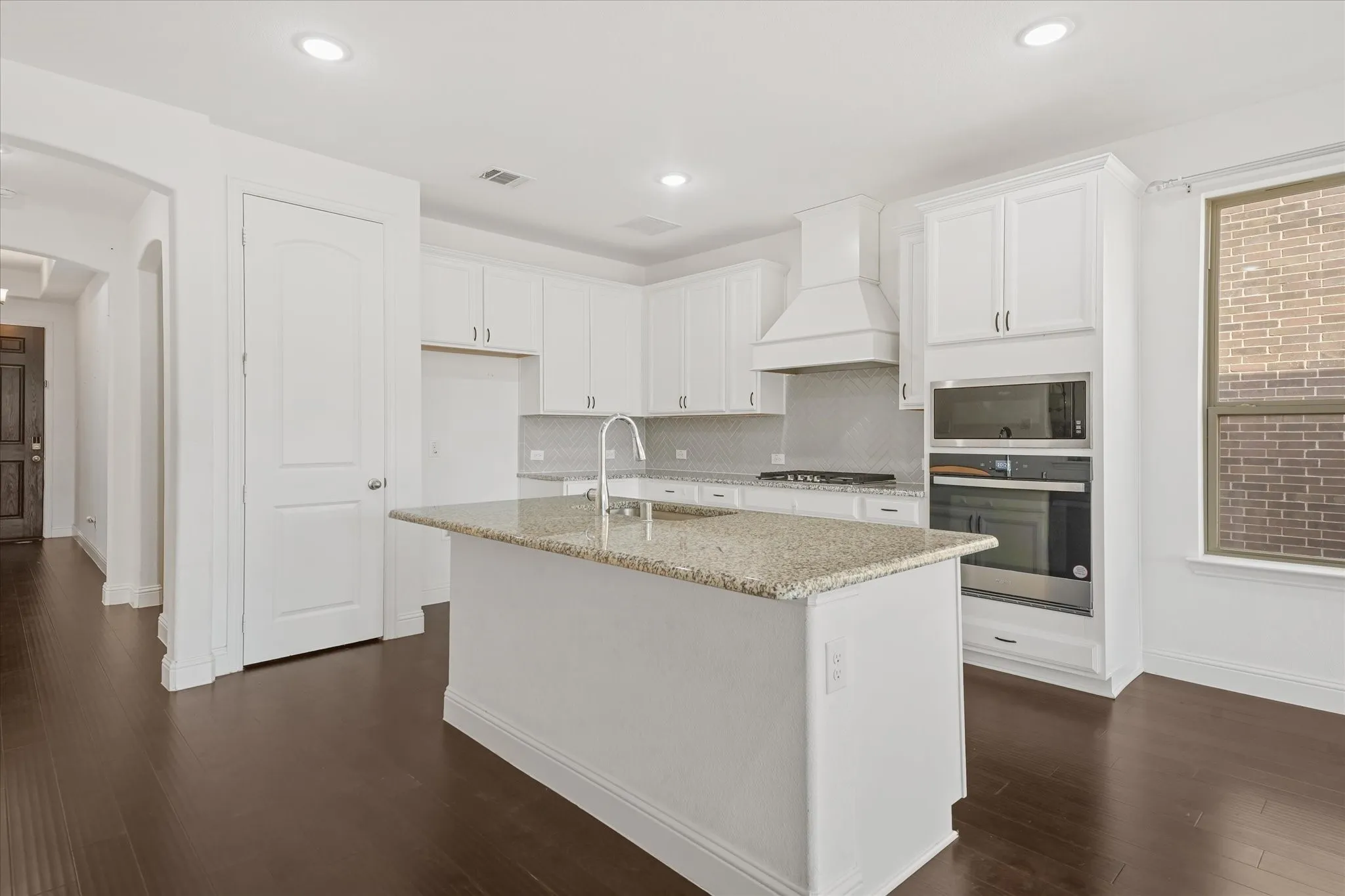 Kitchen featuring white cabinetry, built-in stainless steel appliances, a center island with a light-toned countertop, and dark wood-finish flooring