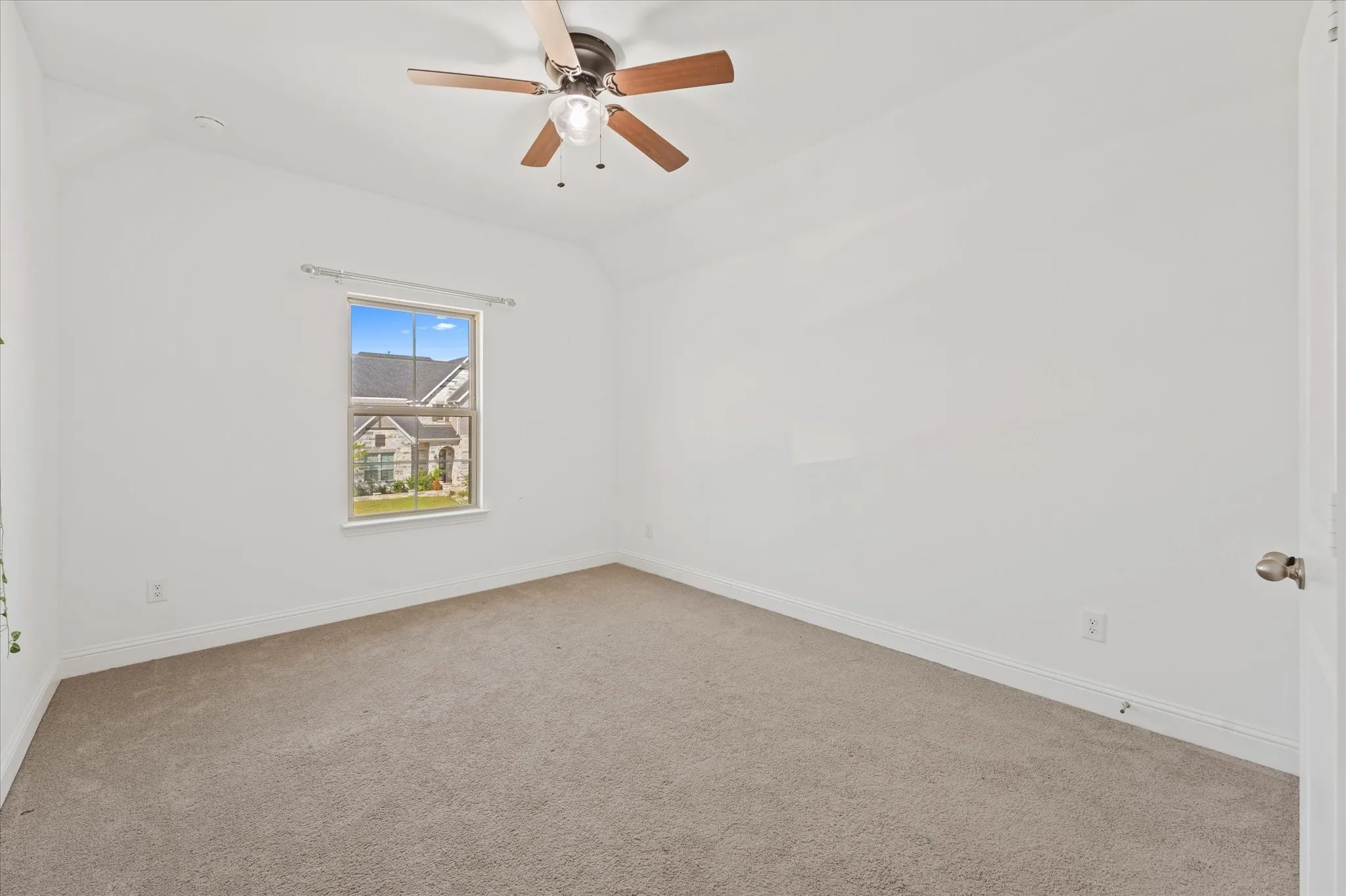 Neutral tone wall finish, window with white trim, ceiling fan with light fixture, and neutral tone carpet