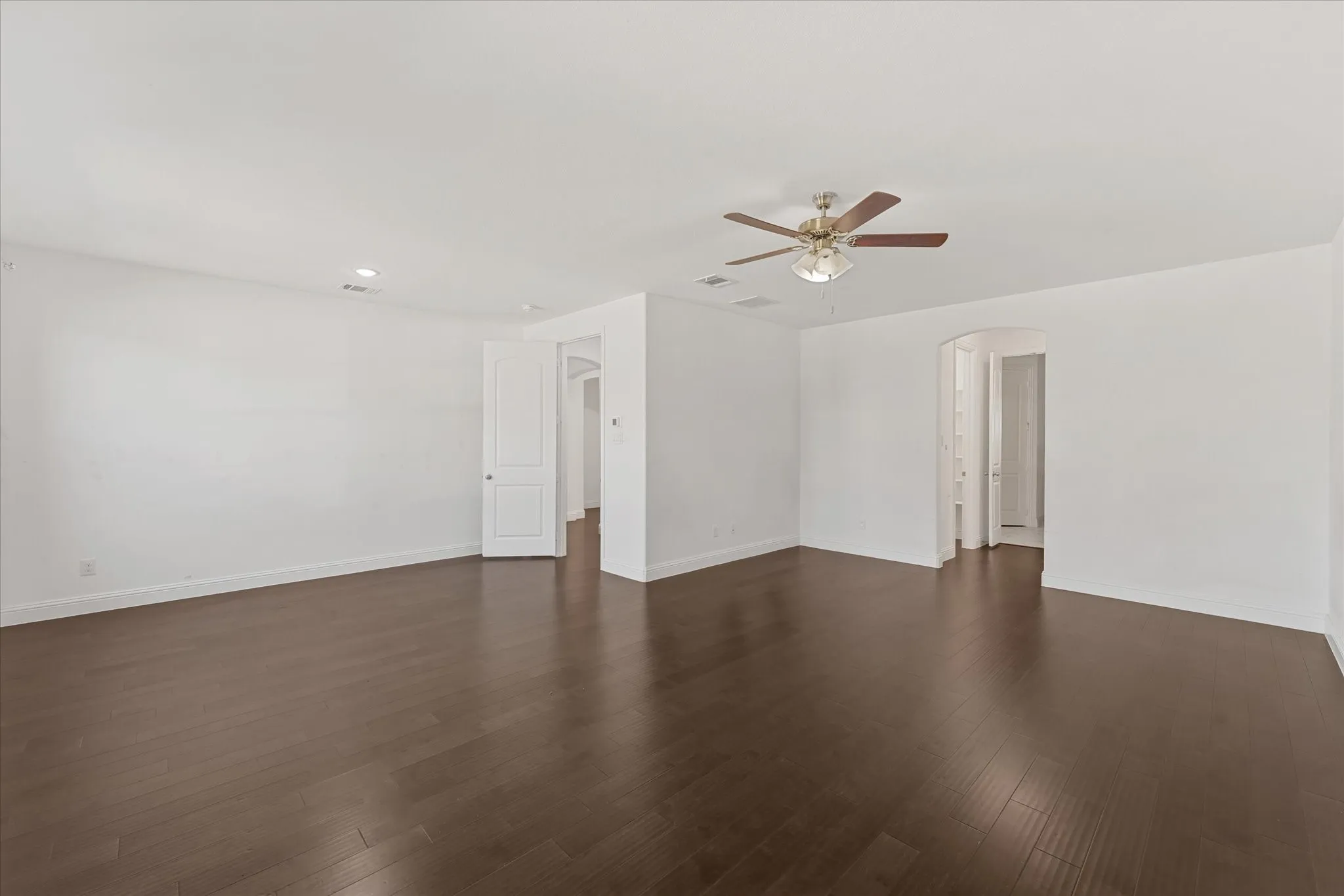 Expansive interior space featuring wood-finish flooring, white walls, a ceiling fan, and recessed lighting