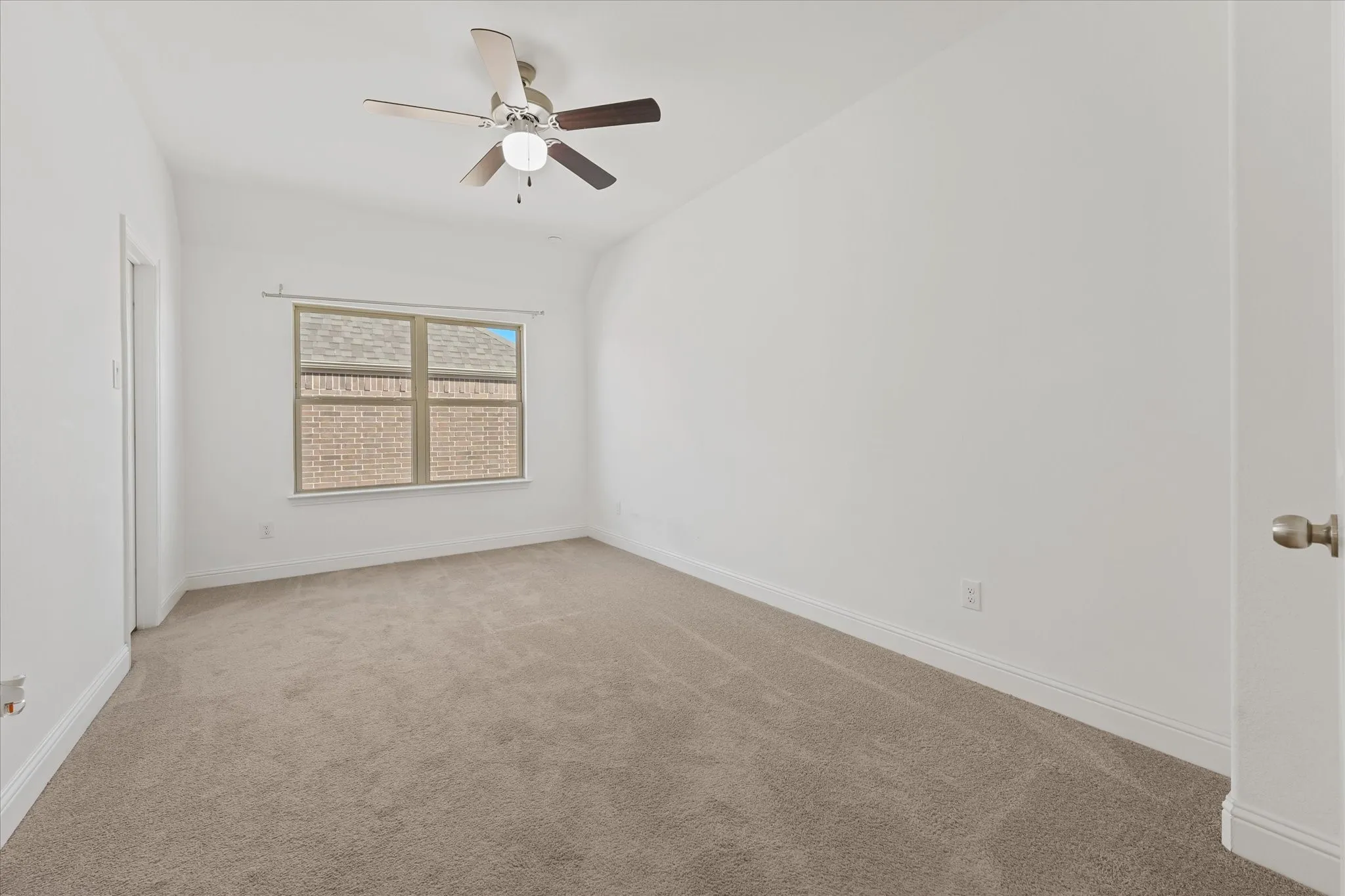 Spacious room featuring neutral carpet flooring, a window with exterior brick detail, and a ceiling fan with integrated lighting
