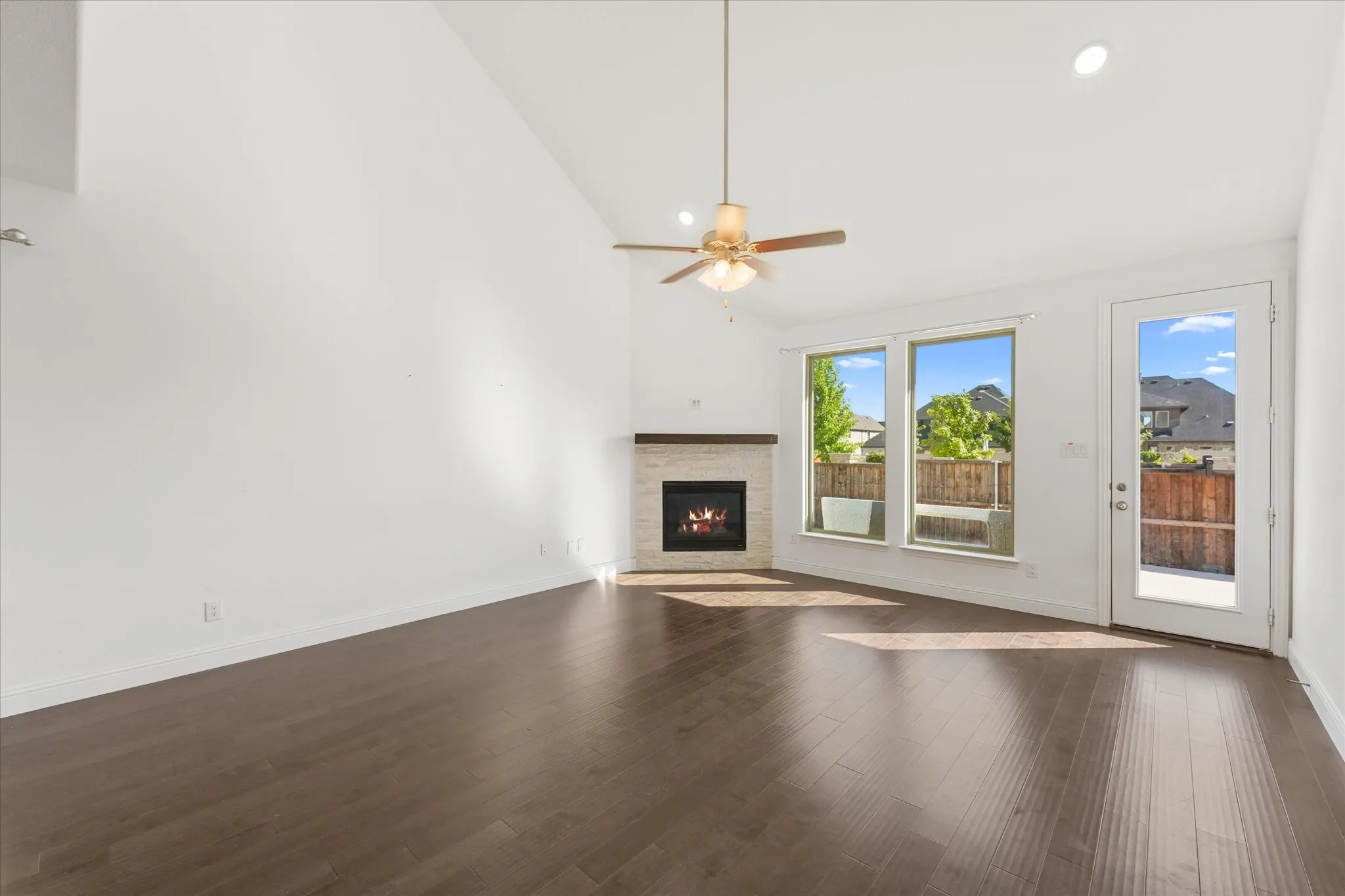 Vaulted ceiling, dark wood-finish flooring, recessed lighting, corner fireplace with wood mantel, and a ceiling fan with integrated lighting