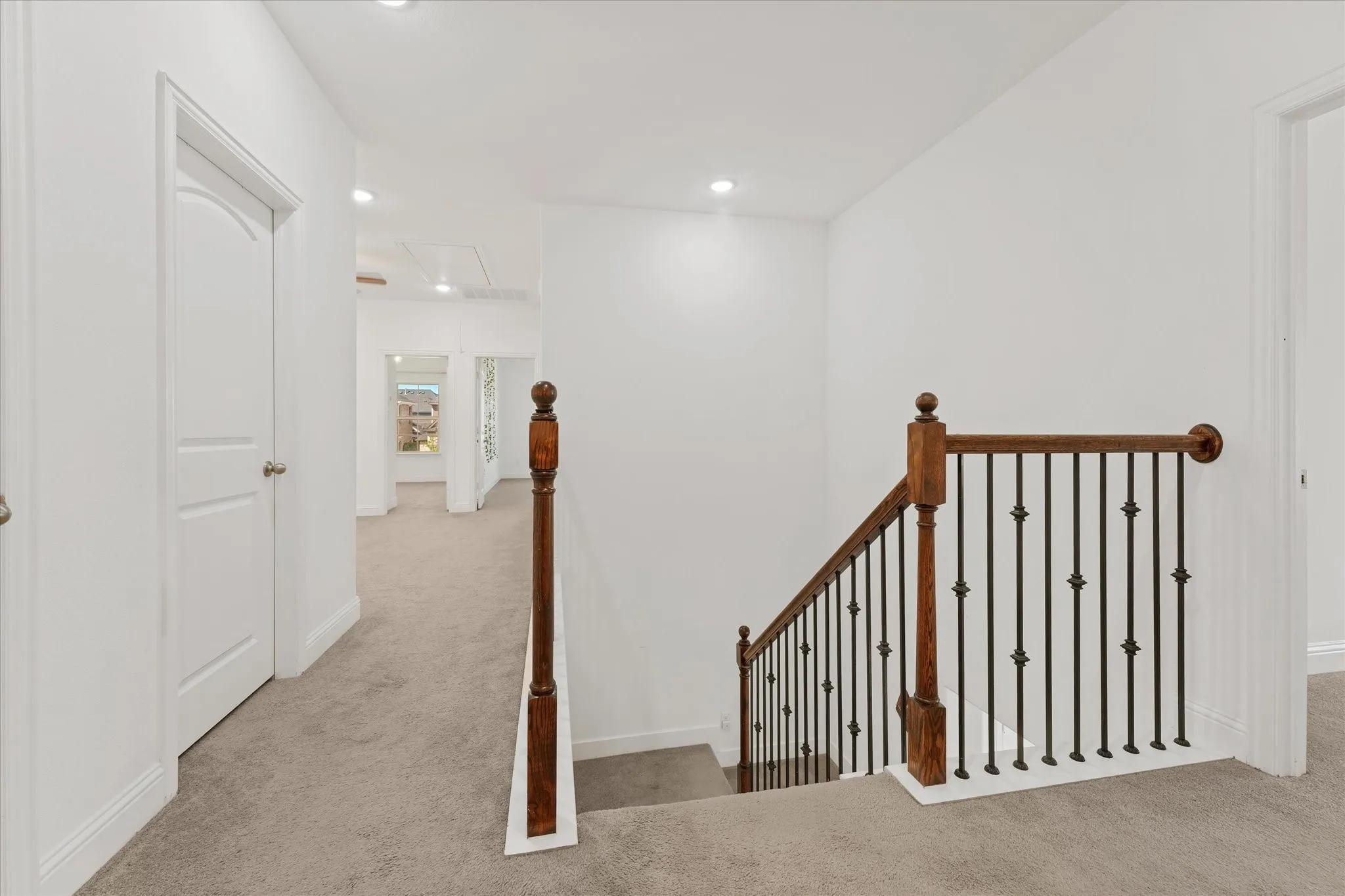 Staircase featuring wood handrails and wrought iron balusters, recessed lighting, white doors with arched panels, and neutral-toned carpeting