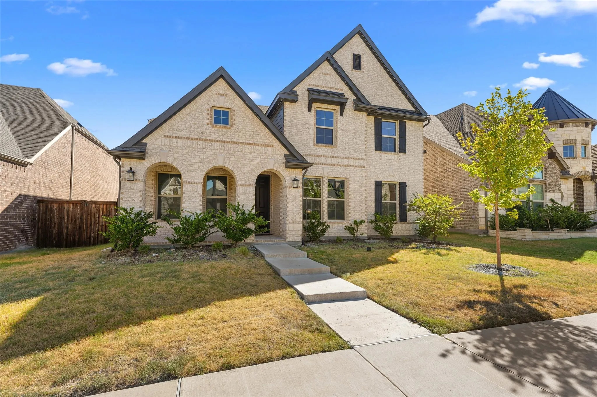Light-colored brick exterior featuring dark trim, arched entryway, and dark shutters