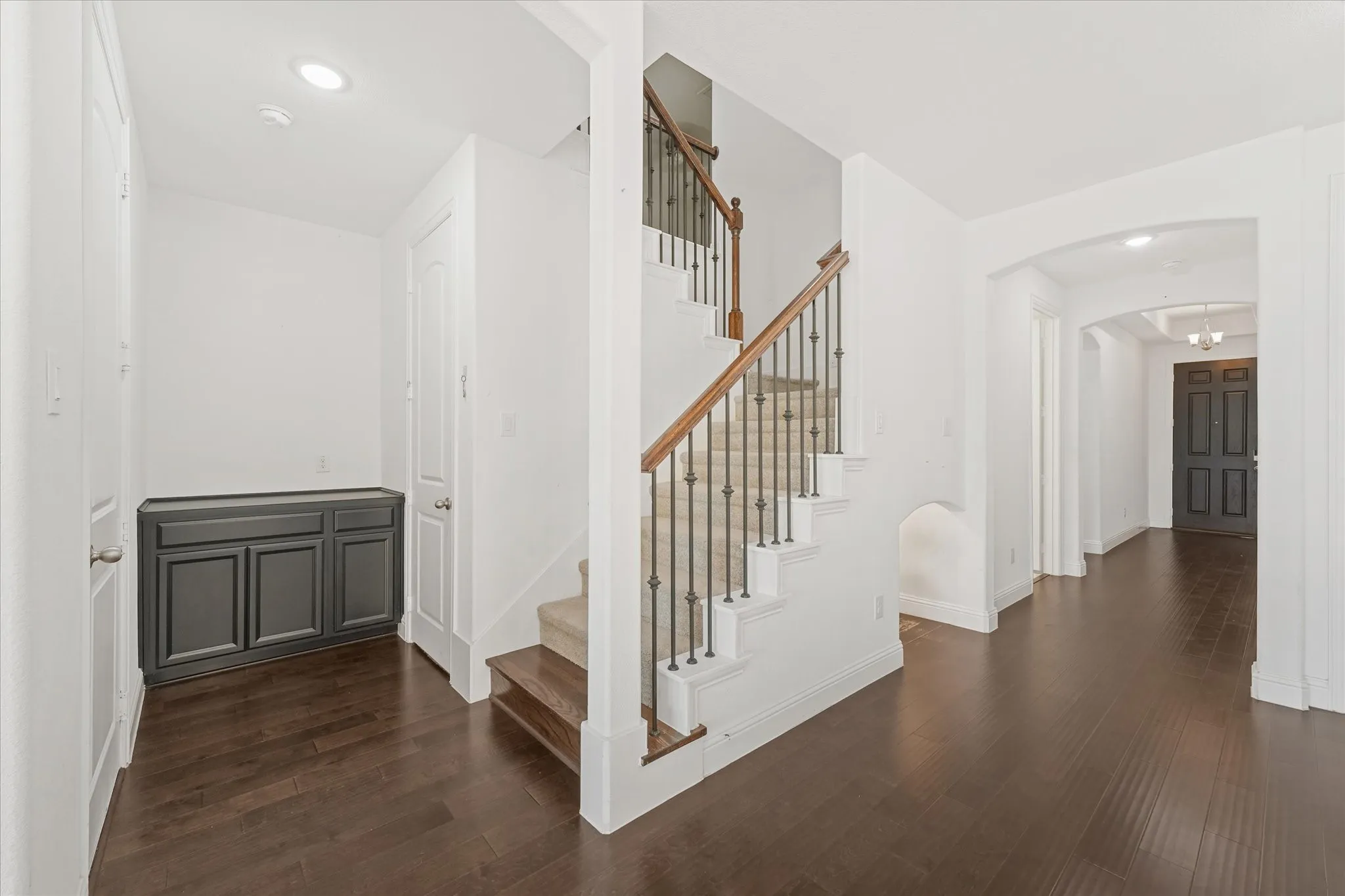 Wood-finish flooring, staircase with wrought iron balusters and wood handrail, recessed lighting, and built-in cabinetry