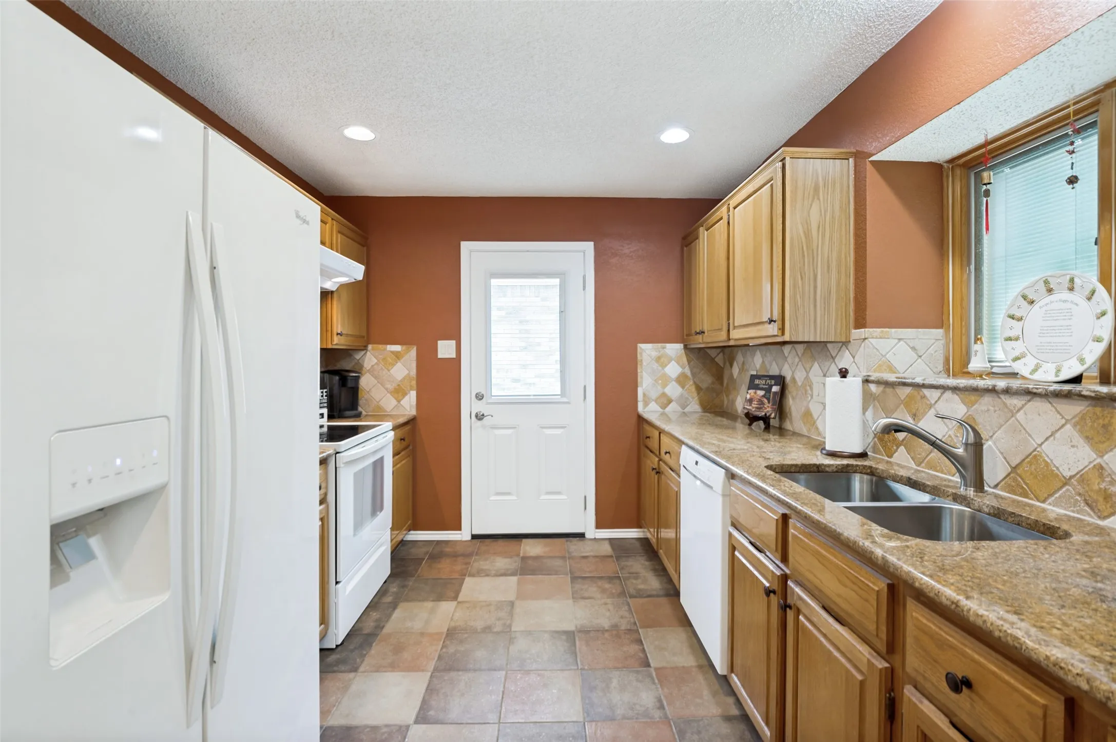 Kitchen featuring wood-finish cabinetry, a double basin stainless steel sink, tiled countertops, a tiled backsplash, and recessed lighting