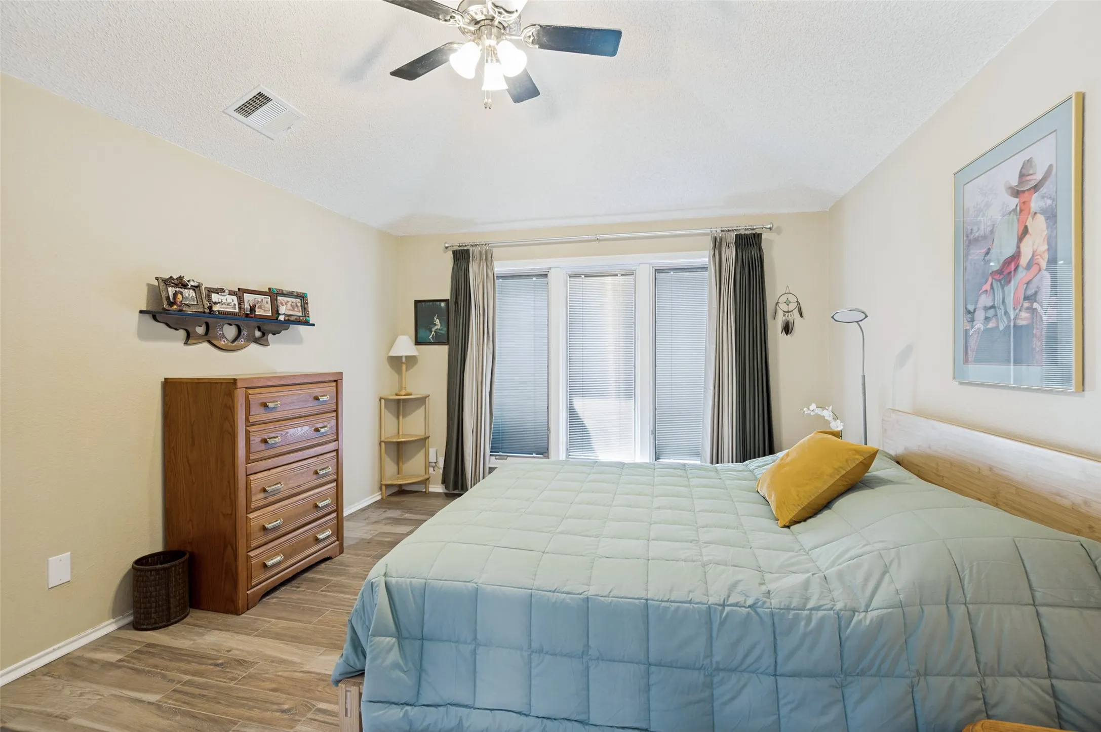 Wood-finish flooring, ceiling fan, and large windows with blinds and curtains