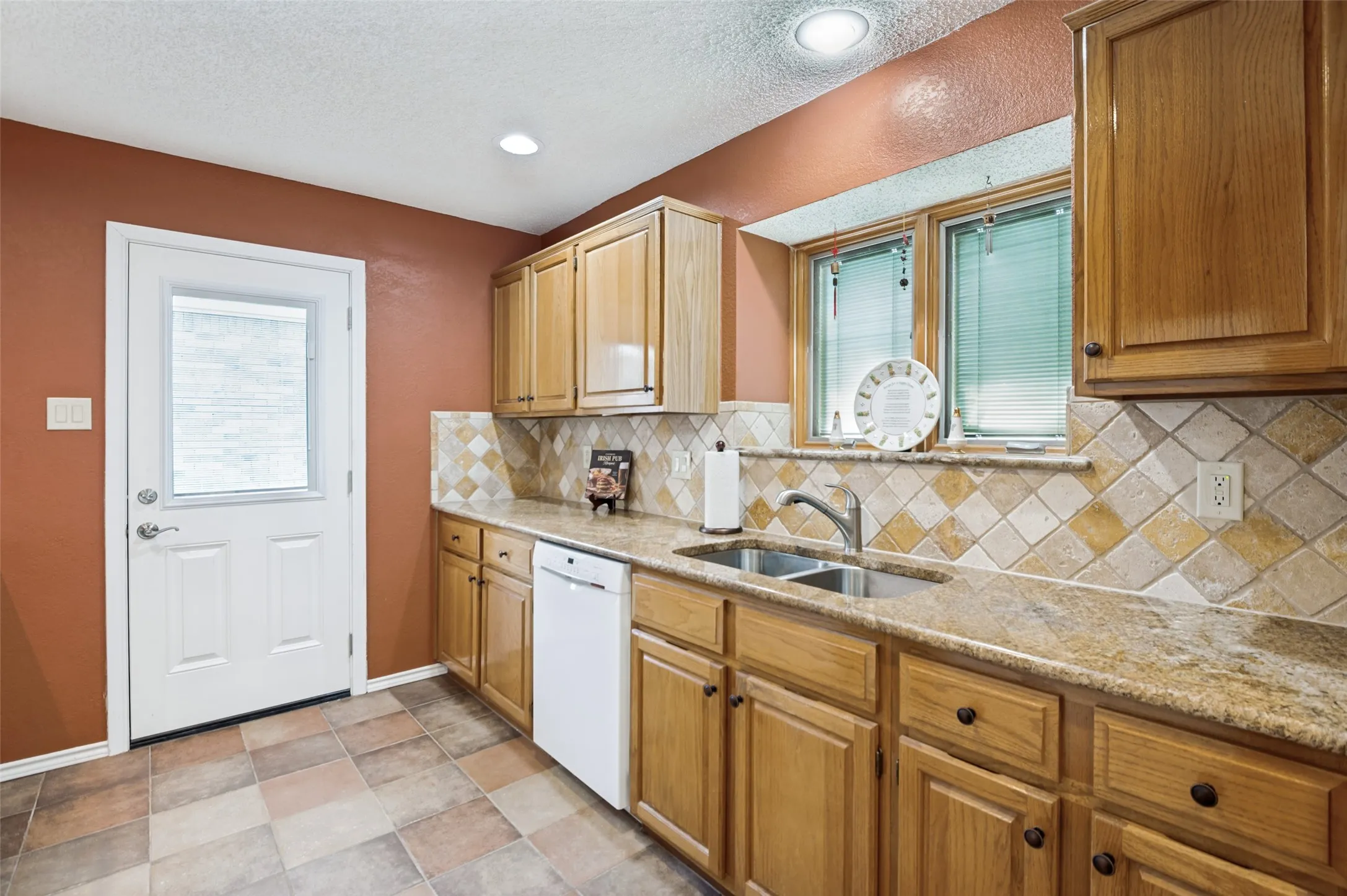 Kitchen featuring wood cabinetry, stone countertops, a tile backsplash, stainless steel sink, and durable tile flooring